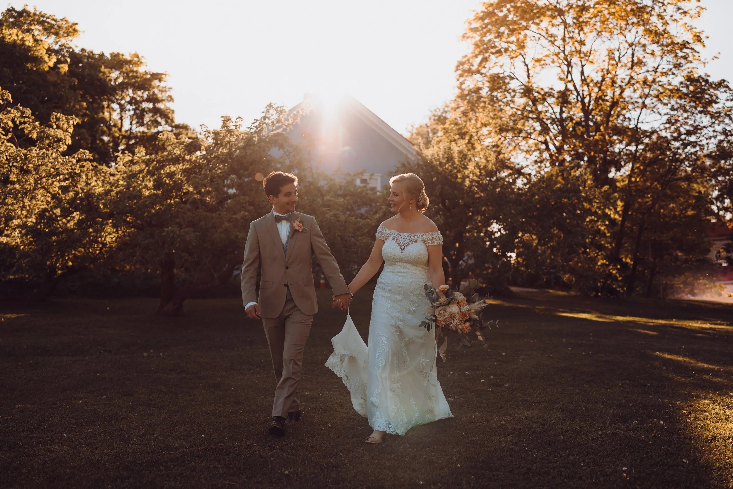 Bride and groom walking hand in hand in a sunlit garden.