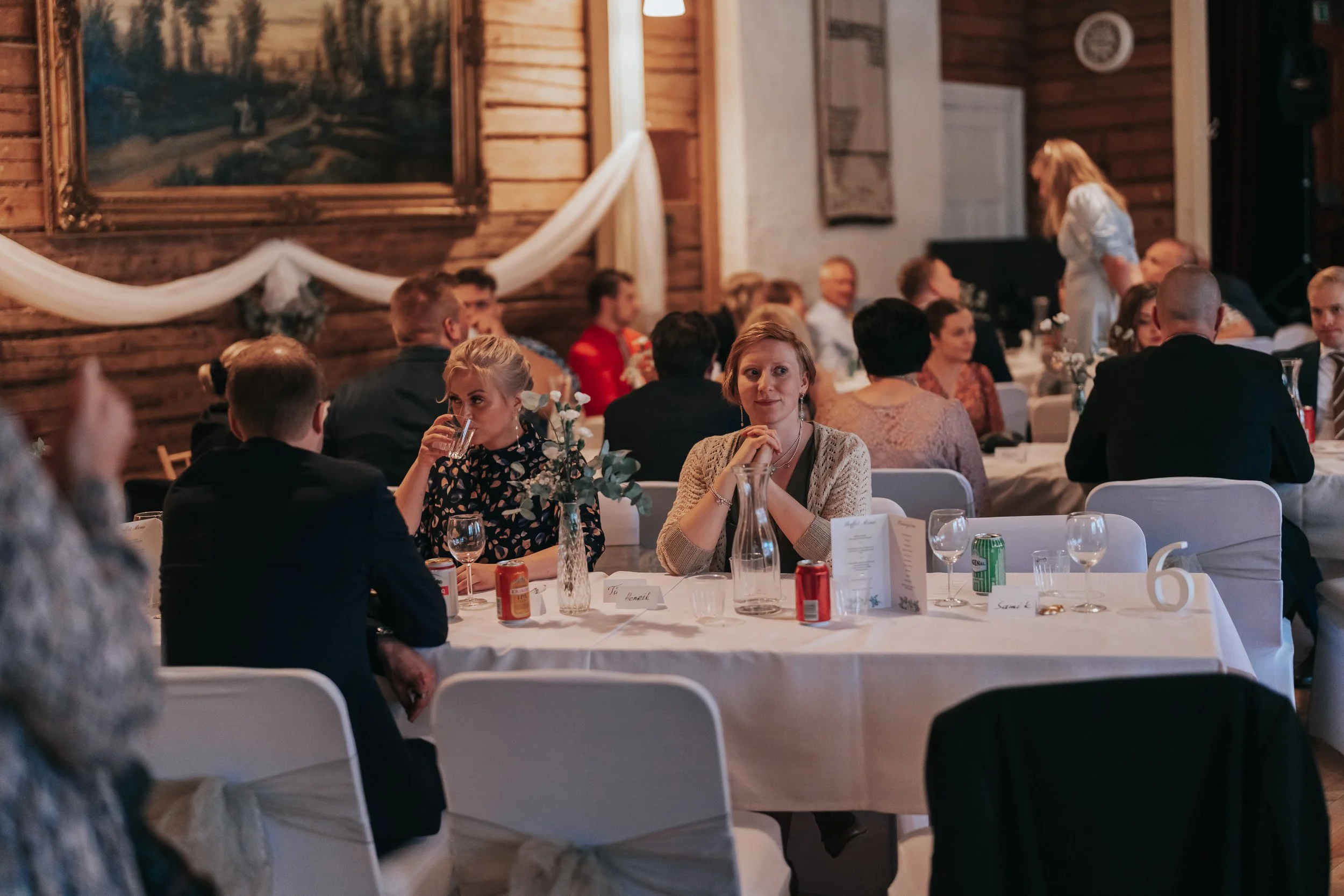 People sitting at tables in a formal event setting with white tablecloths, drinks, and decorations.