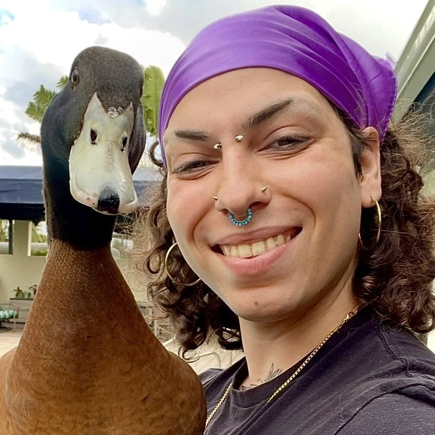 A smiling person with a purple bandana posing with a duck.