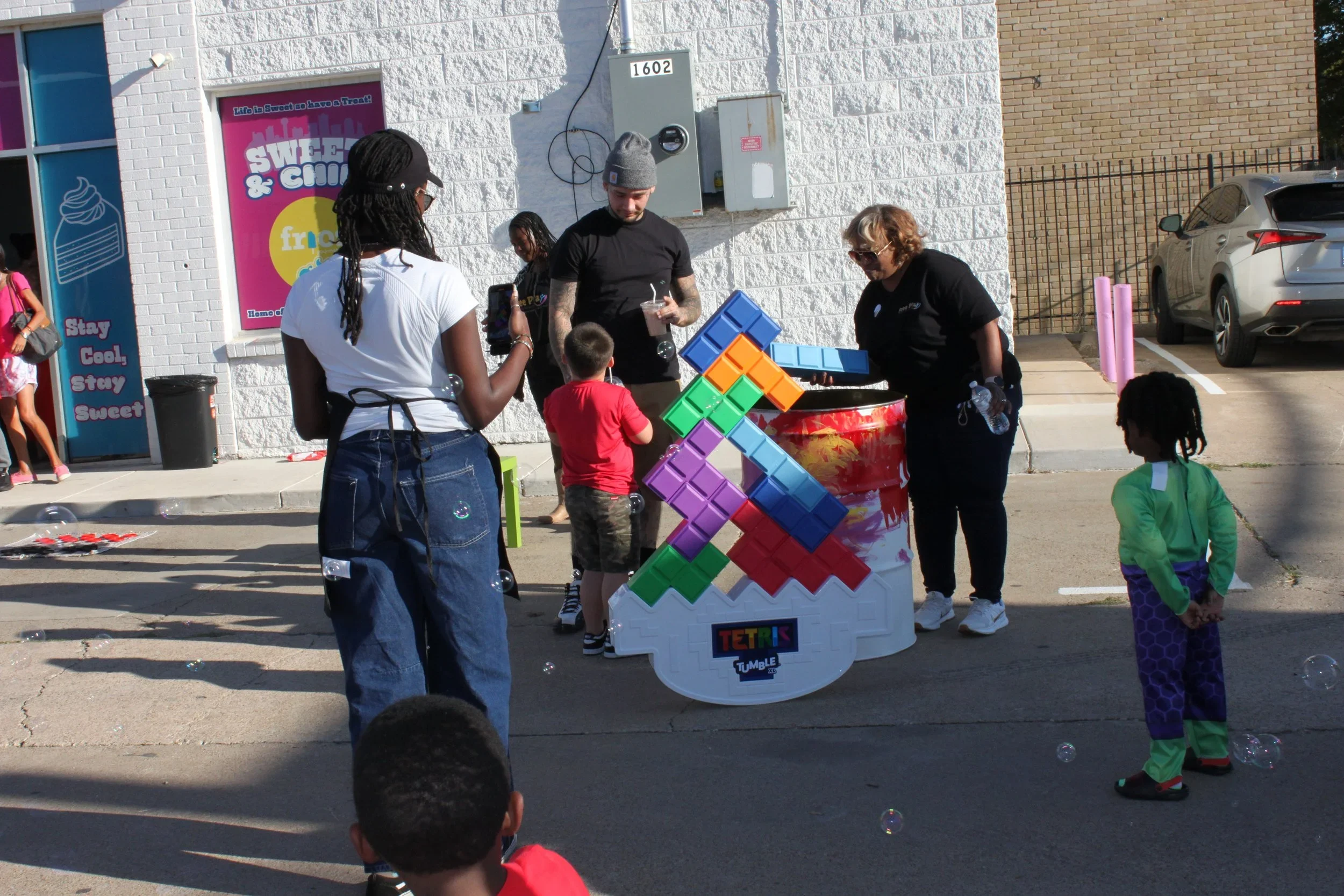 A man giving a presentation or speech to a group of people seated at a long table in a covered outdoor patio area decorated with string lights.
