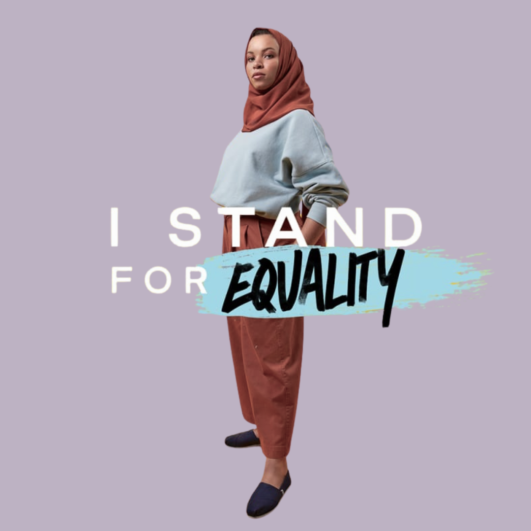 A woman wearing a burnt orange hijab, grey oversized sweatshirt, and matching burnt orange pants standing with her hand in her pocket over a lavender background. Text on the image reads 'I stand for equality' with 'equality' in bold black font on a blue brushstroke.