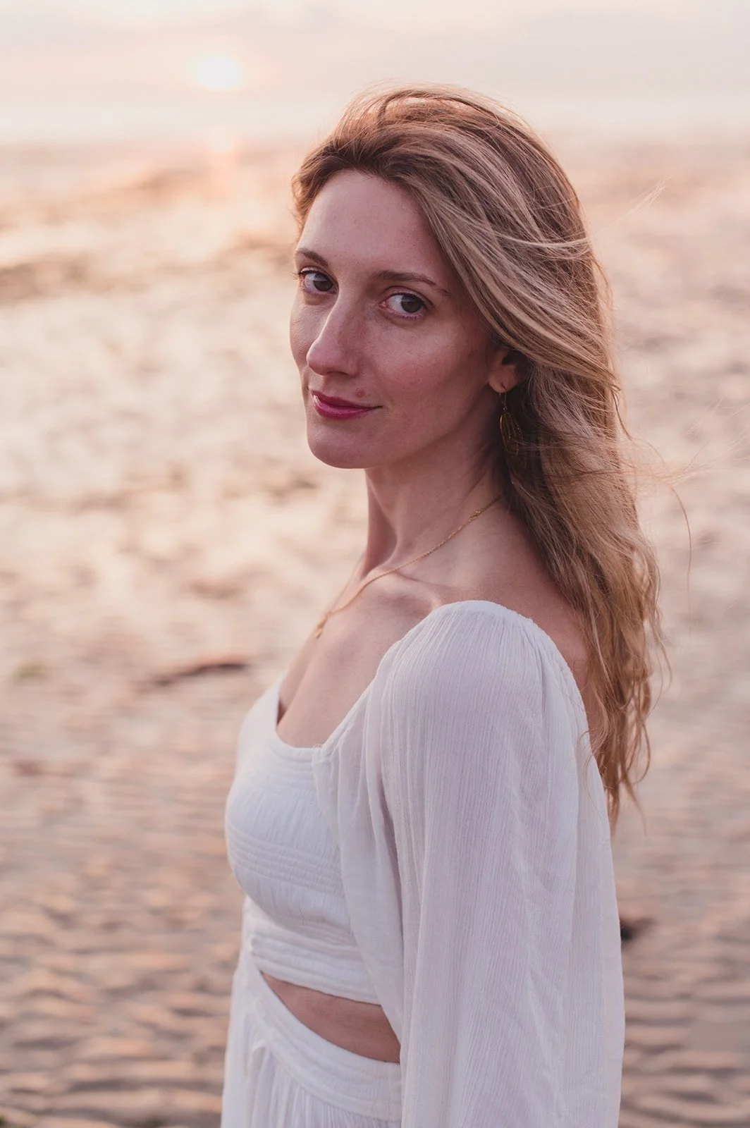 Woman in white dress with soft wavy hair, elegant and serene.