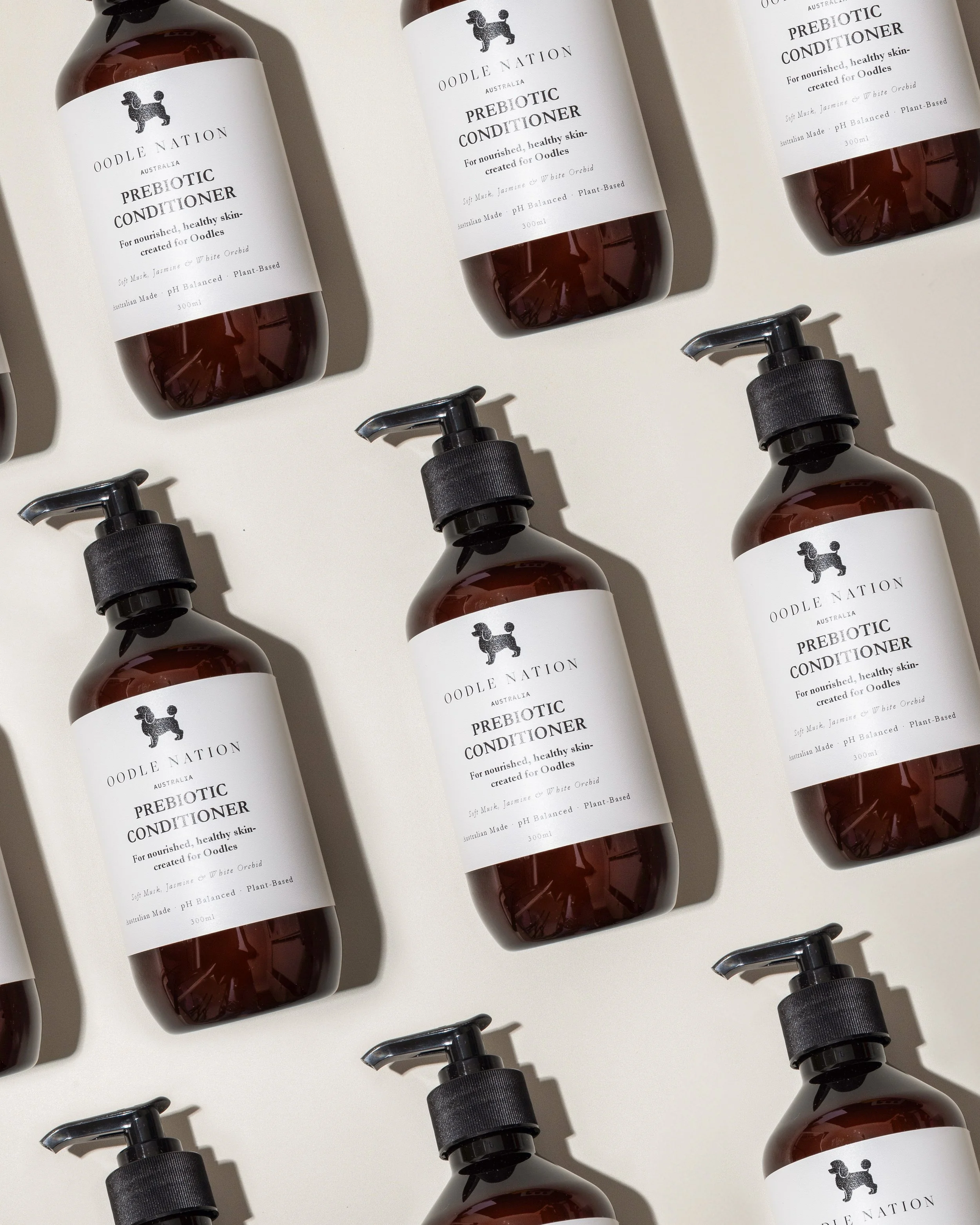 Multiple bottles of Oodle Nation prebiotic conditioner for pets arranged on a light surface, with some bottles lying on their sides and pump dispensers visible.