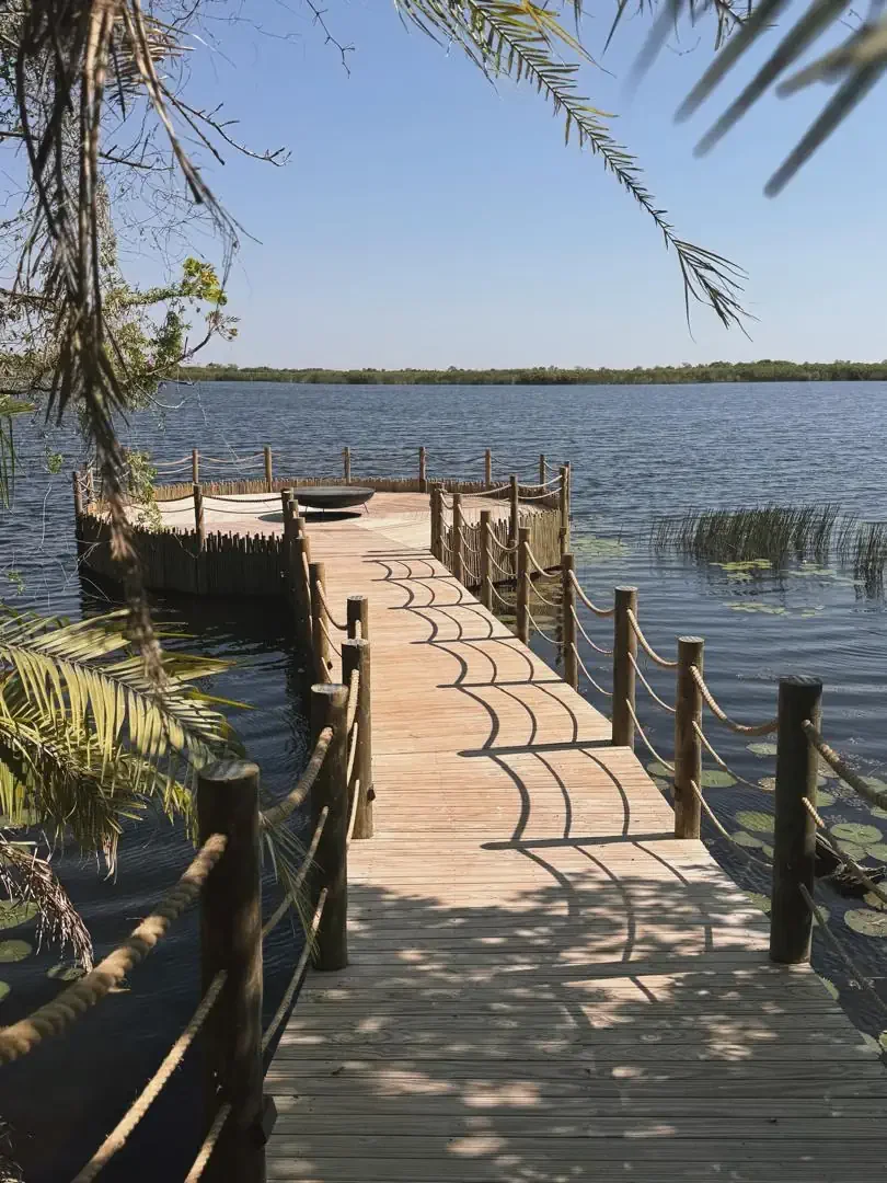 A wooden boardwalk extending over a tranquil river leading to a viewing deck at a luxury African safari lodge