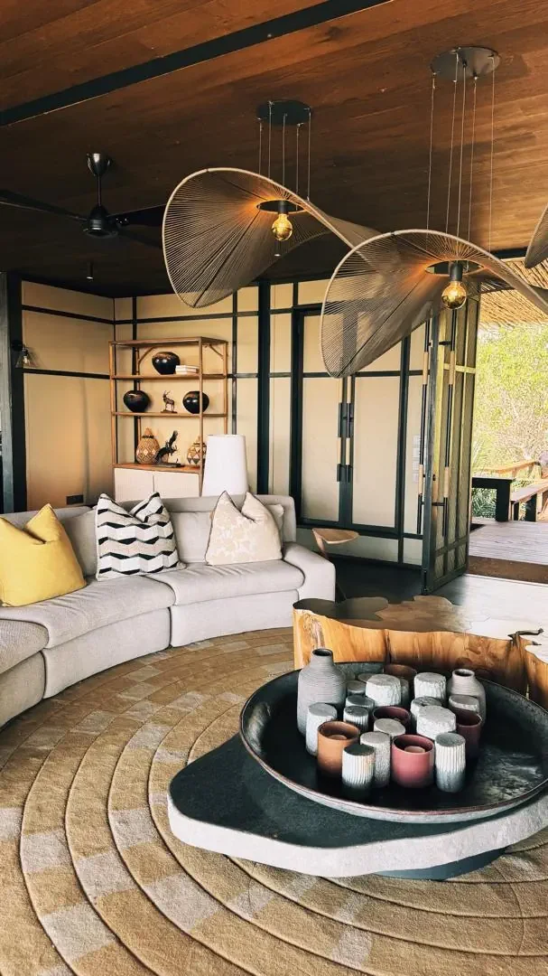 The elegant interior lounge area of a luxury African safari lodge featuring a plush sofa, statement lighting, and contemporary natural design elements