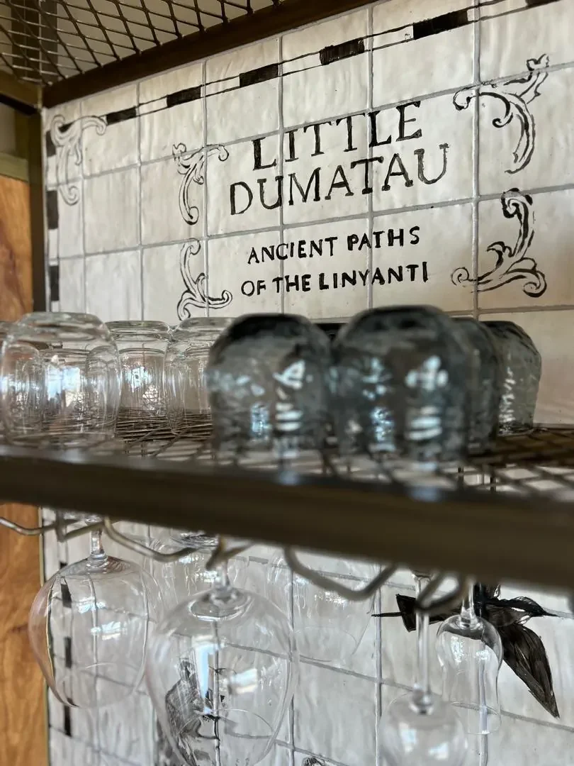 A decorative tiled sign for Little DumaTau camp above drinking glasses at a luxury African safari lodge