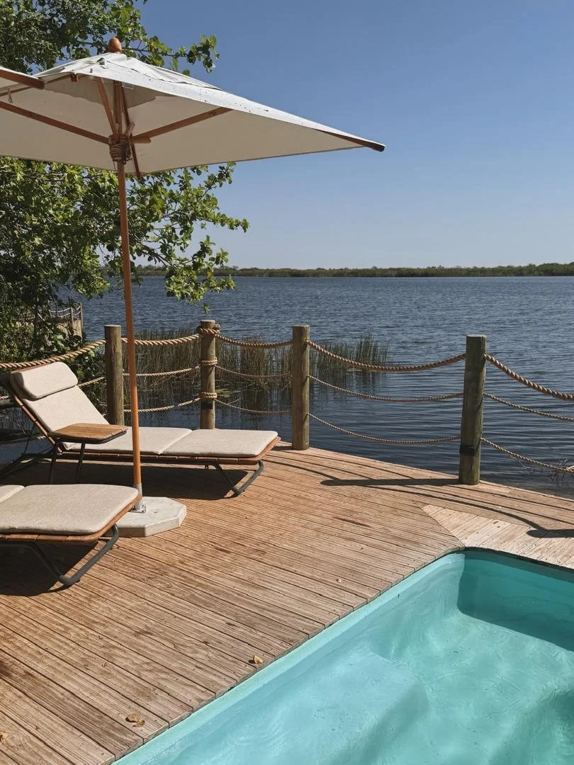 Lounge chairs on a wooden deck next to a plunge pool overlooking a serene river at a luxury African safari lodge