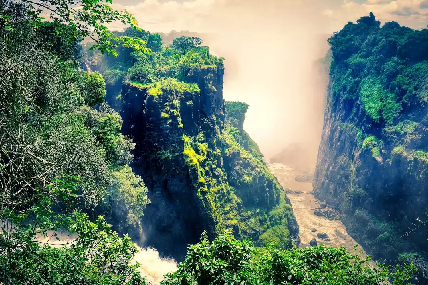 Lush green cliffs surrounding the thunderous mists of Victoria Falls in Zimbabwe.