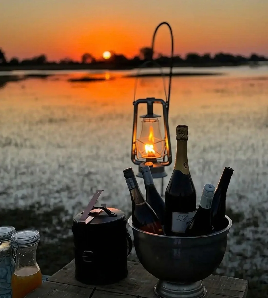 A romantic setup with chilled wine in an ice bucket and a glowing lantern by the water at sunset for an African honeymoon safari