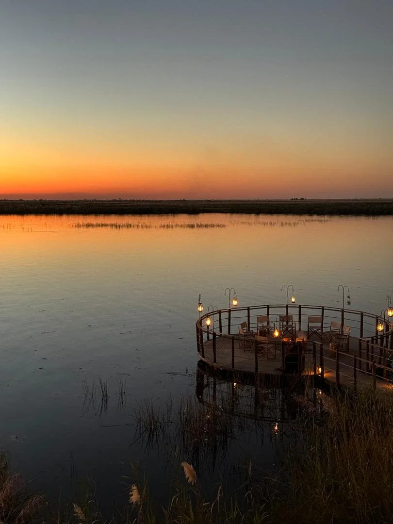 A circular wooden deck with glowing lanterns overlooking a calm river at sunset on a luxury African safari