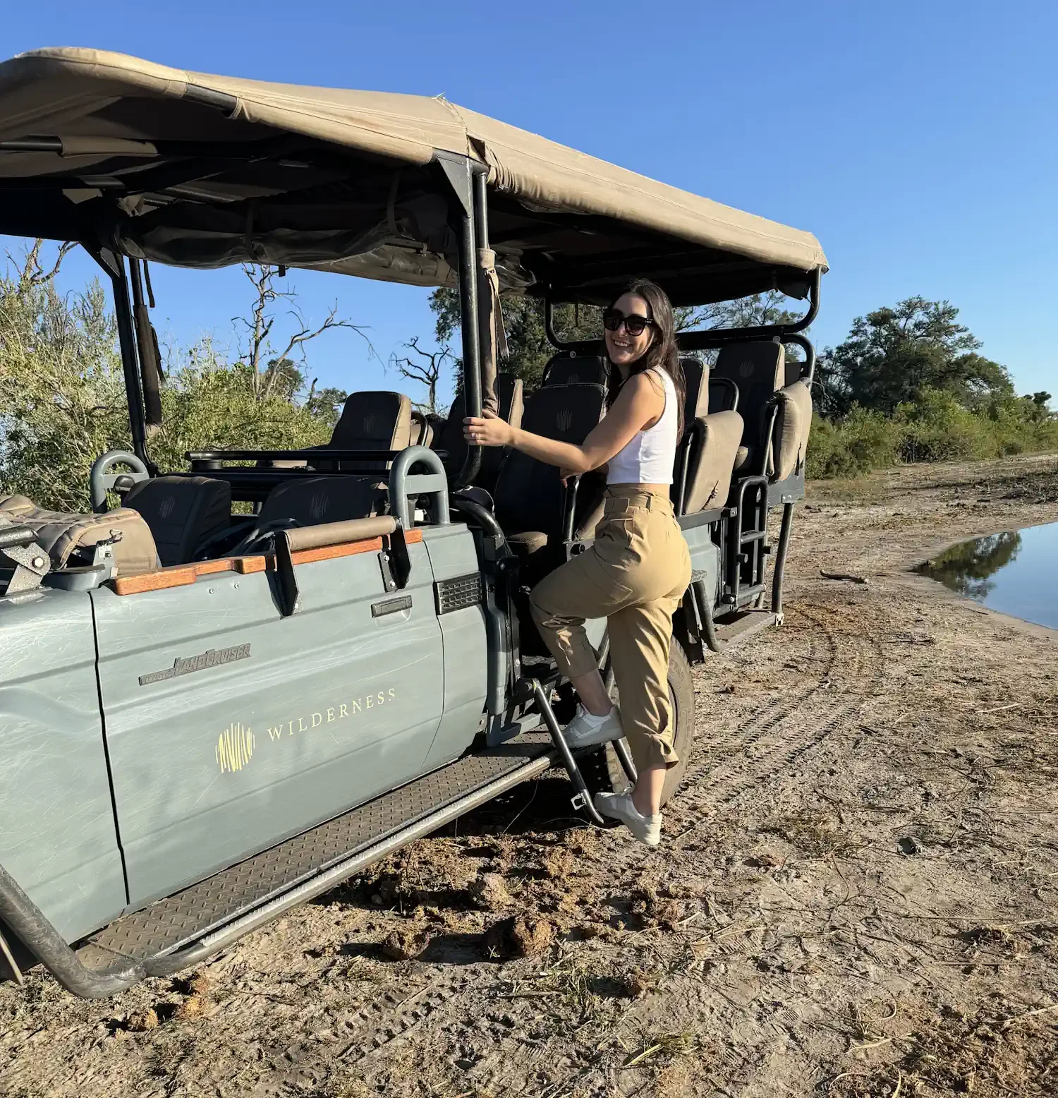 Co-founder Kristy Briscoe smiling as she boards a grey, open-air 4x4 safari vehicle near a body of water.