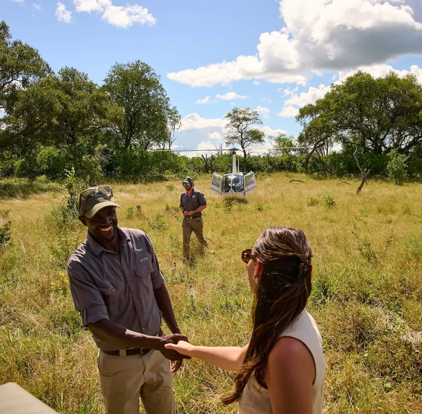 Beyond the Baobab co-founder Kristy Briscoe smiling and shaking hands with a local Botswana safari guide after a private helicopter landing in the Okavango Delta.
