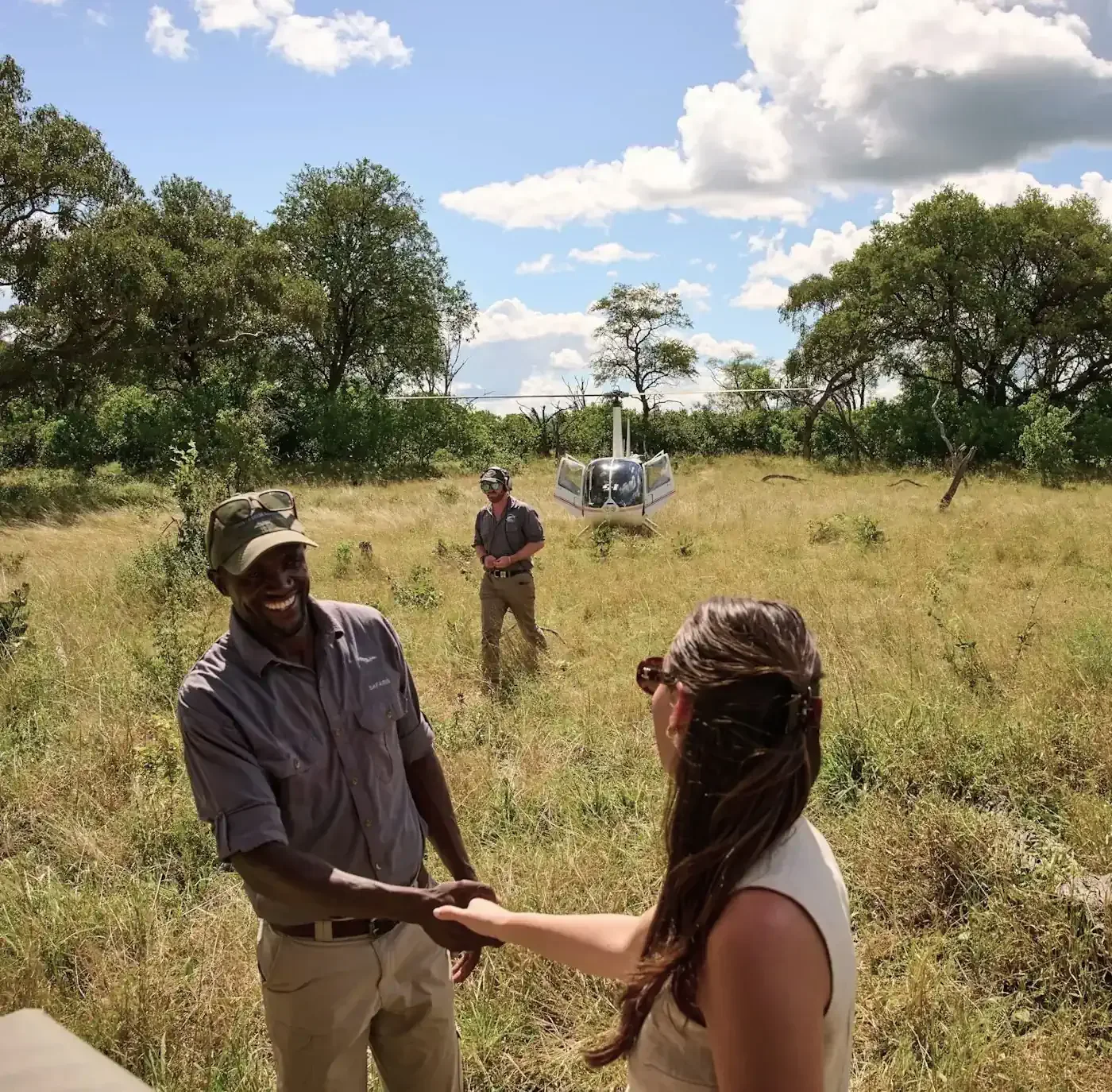 A guest shaking hands with a smiling safari guide in the African bush, with a private helicopter waiting in the background for a specialist expedition.