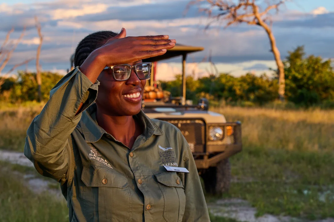 A smiling expert private guide looking out over the bush next to a safari vehicle during a custom African safari journey