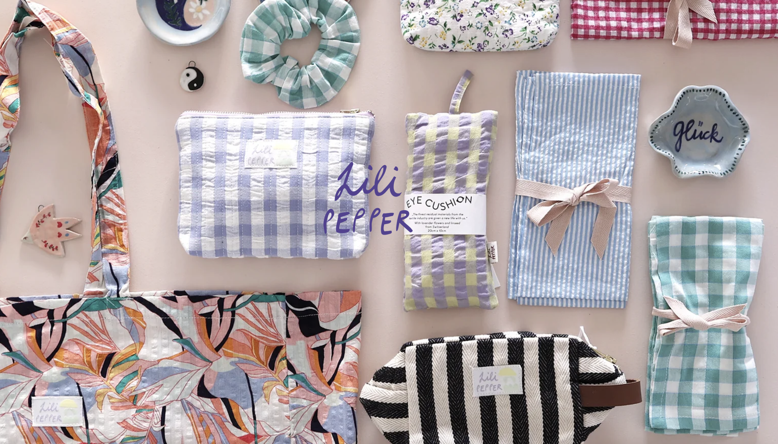 Eine Auswahl an Handwerksprodukten wie Stoffbeutel, Schals, Haarbänder und kleine Keramiken in Pastelltönen auf einem Tisch angeordnet.