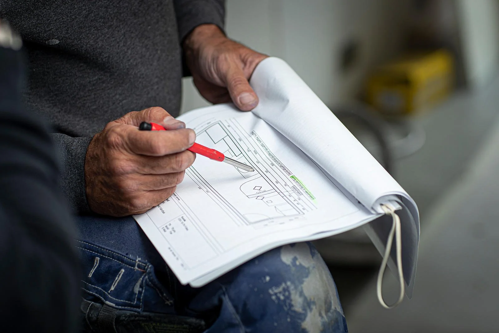 Person som holder en rød penn og ser på en tegning eller plan, med fokus på hendene og dokumentet.