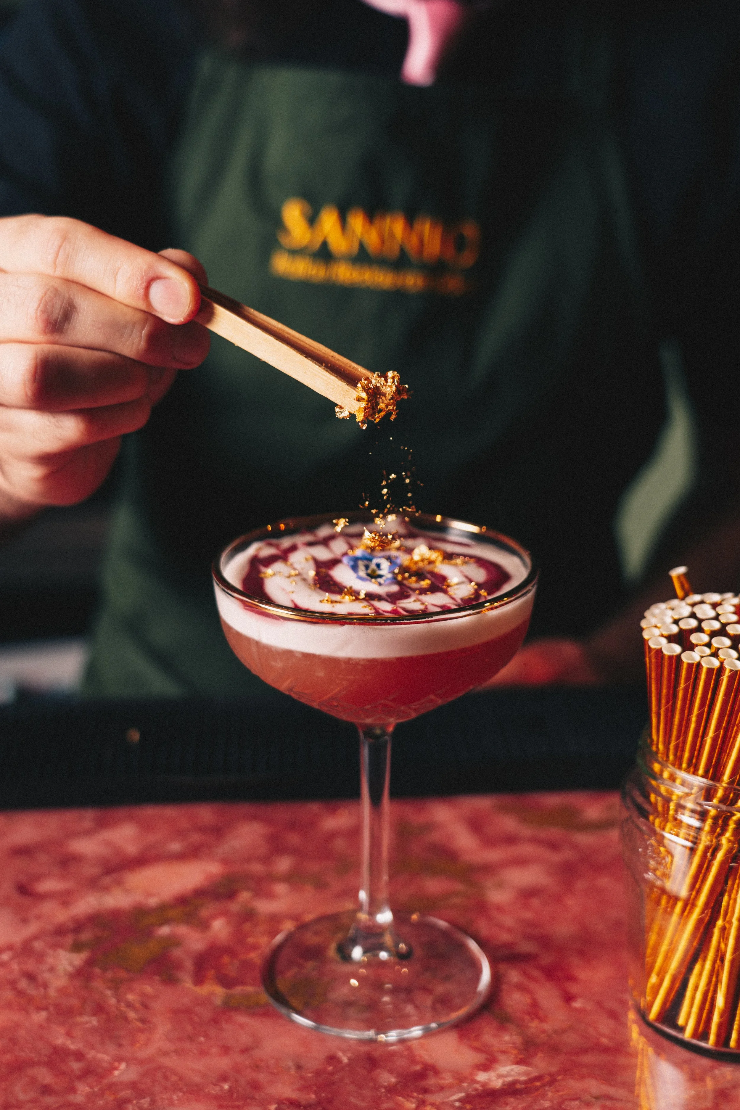 finishing touches of edible gold being added to an expertly crafted martini cocktail