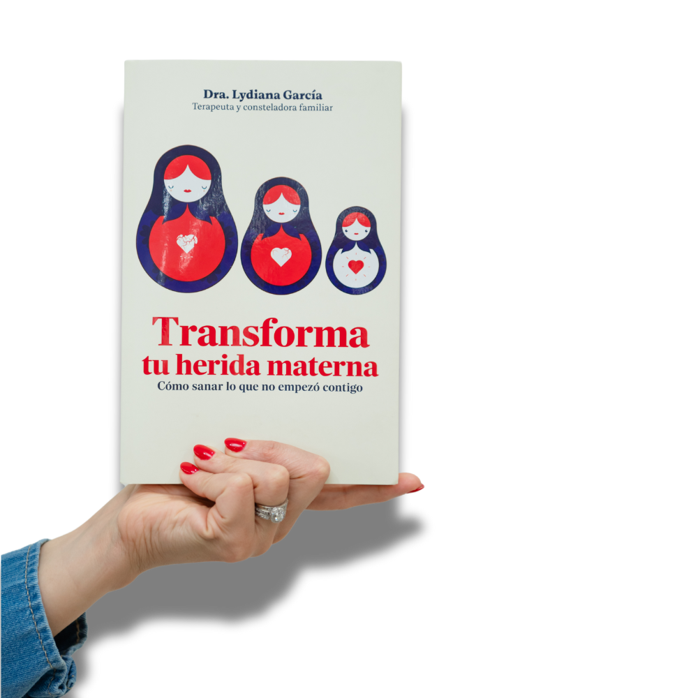 Libro titulado "Transforma tu herida materna" con ilustraciones de figuras femeninas en colores rojo, azul y blanco, y una mano con uñas pintadas de rojo sosteniéndolo.