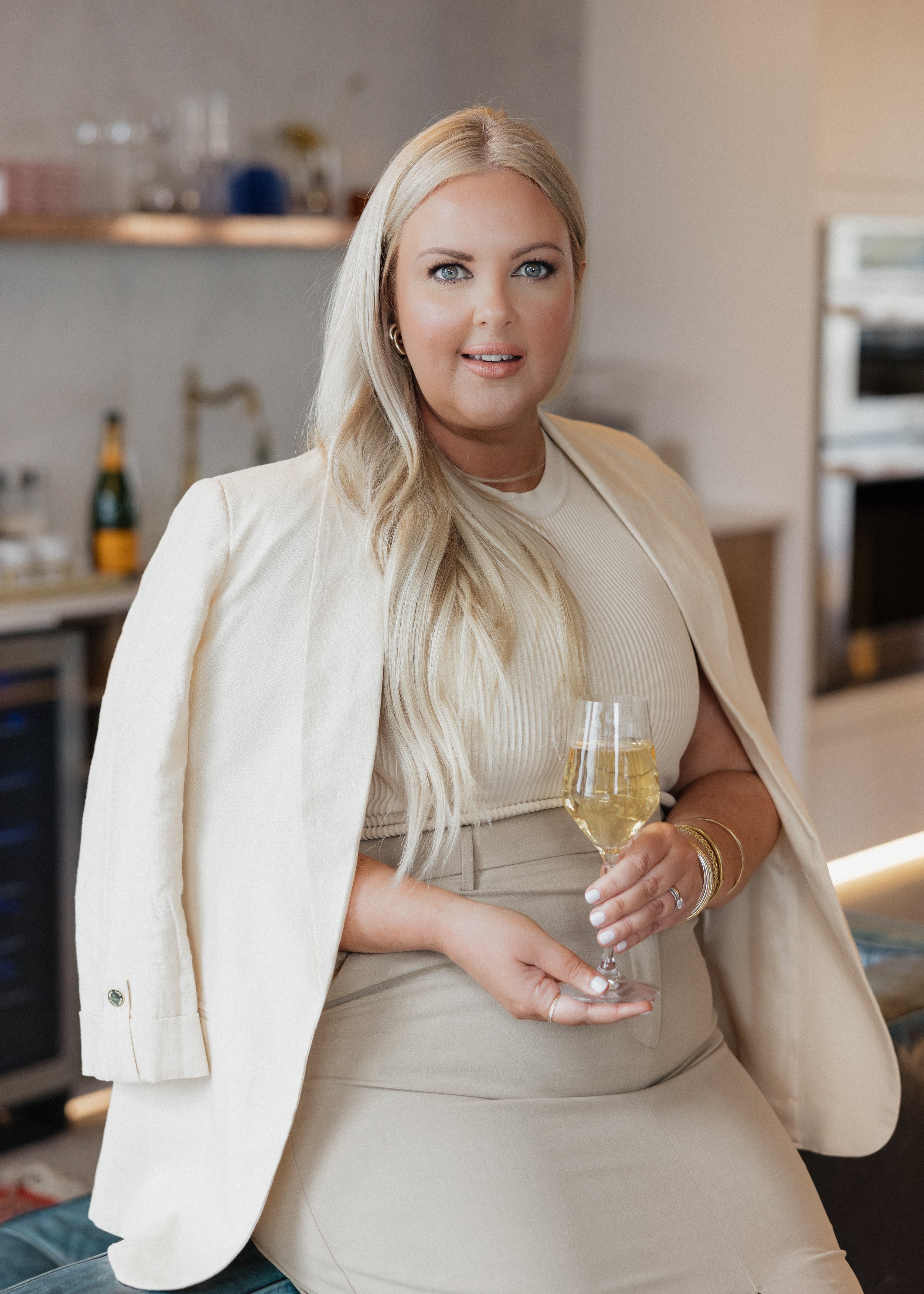 Person with long blonde hair holding a glass of champagne in a modern kitchen.