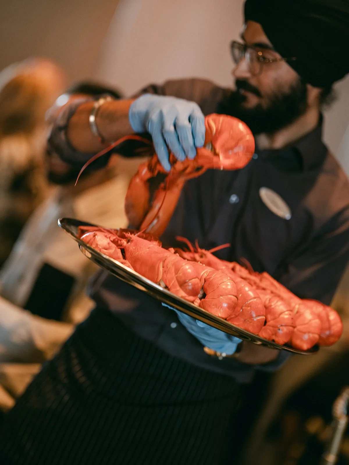Person serving a tray of cooked lobsters at an event.
