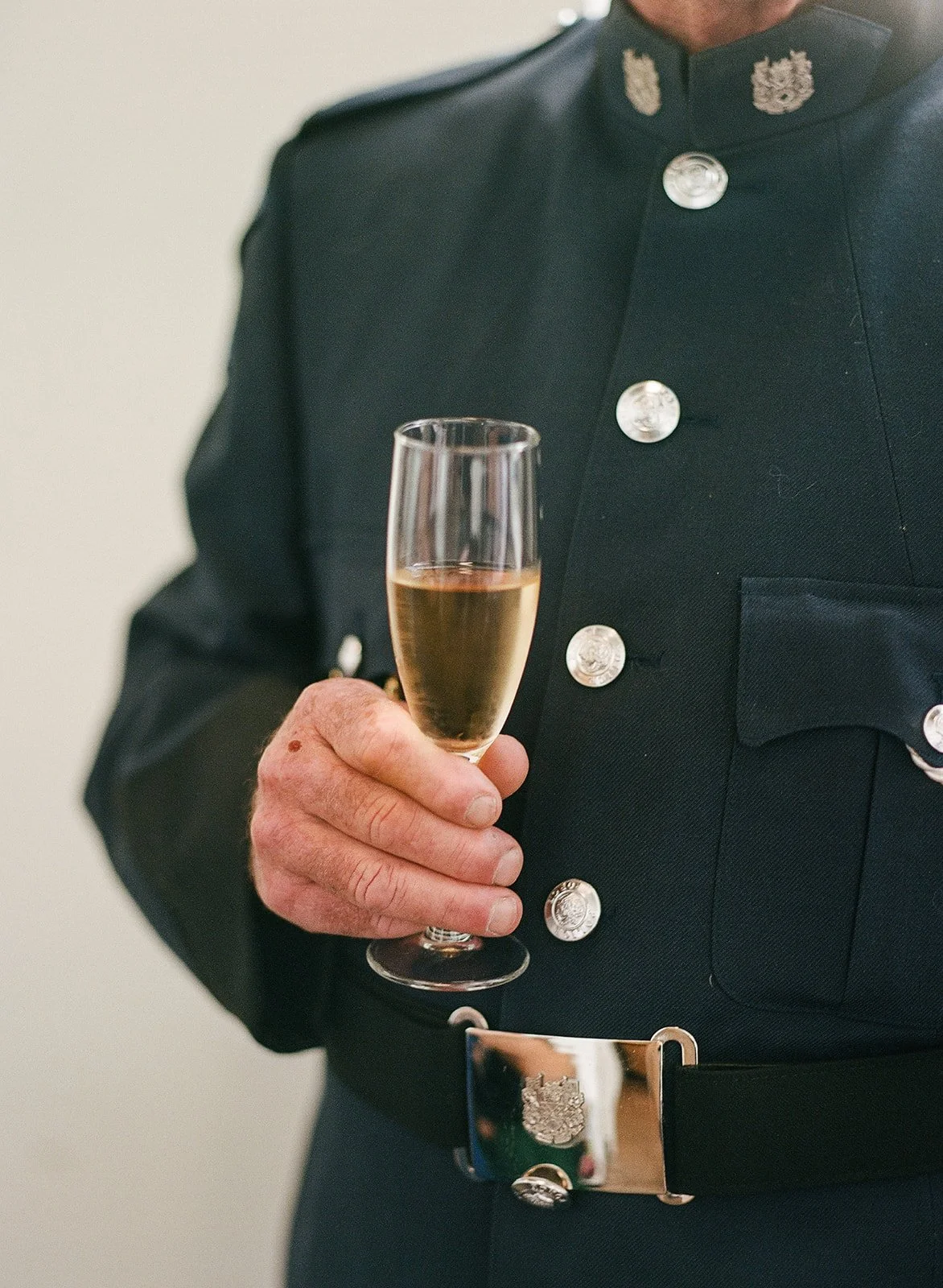 Person in formal military uniform holding a glass of champagne.