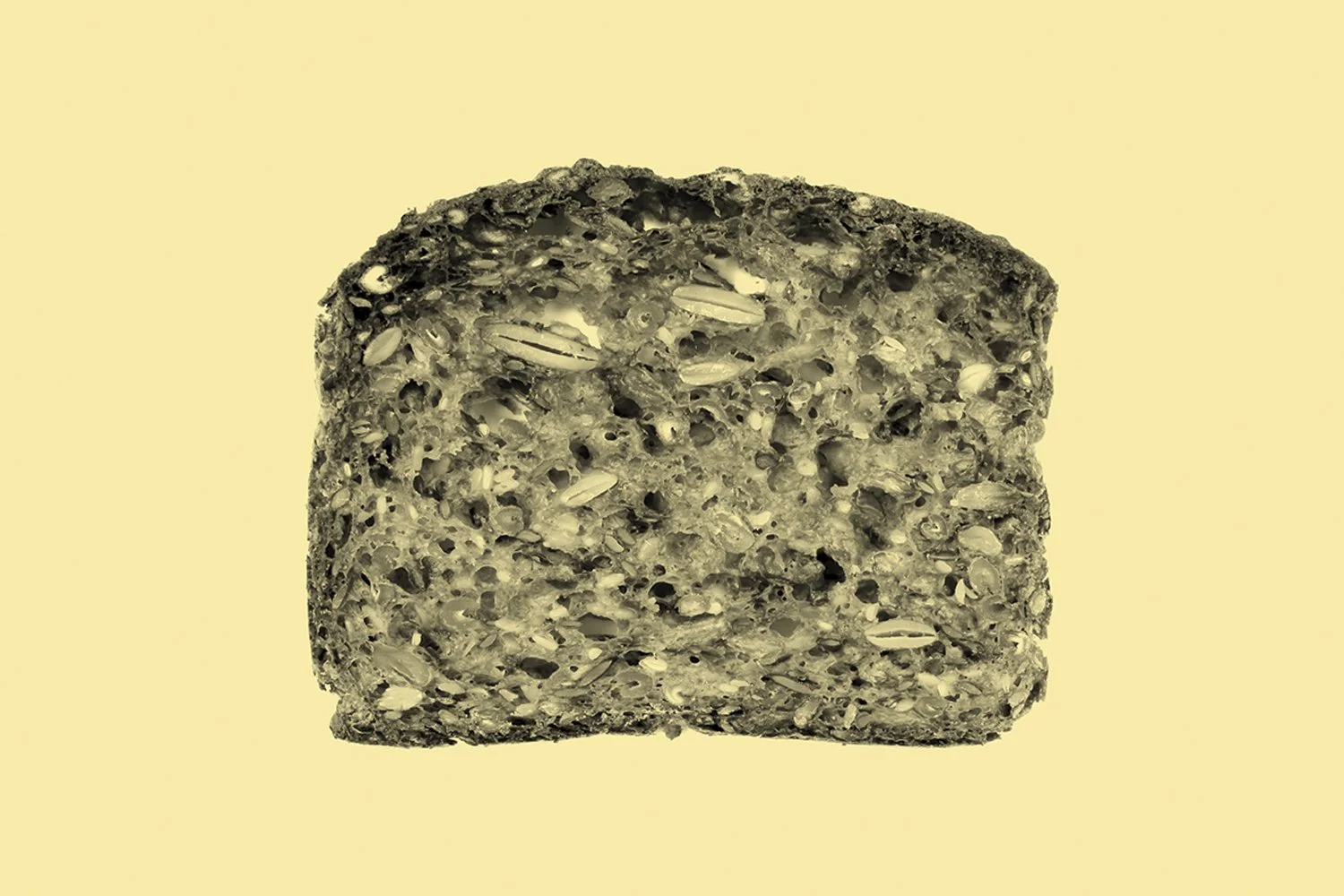 A slice of multigrain bread with seeds and grains visible on the surface, on a light yellow background.