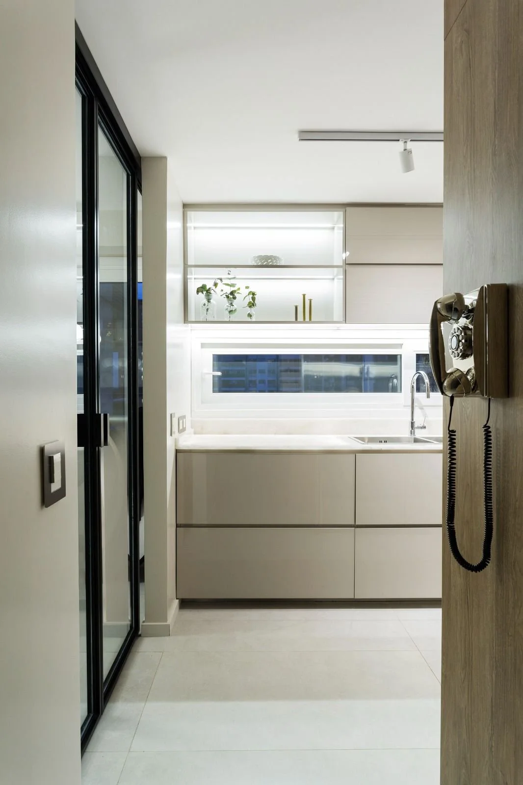 Modern kitchen with white cabinetry, a marble countertop, and a window above the sink. There are decorative items on the shelves and a vintage wall-mounted telephone on a wooden wall.