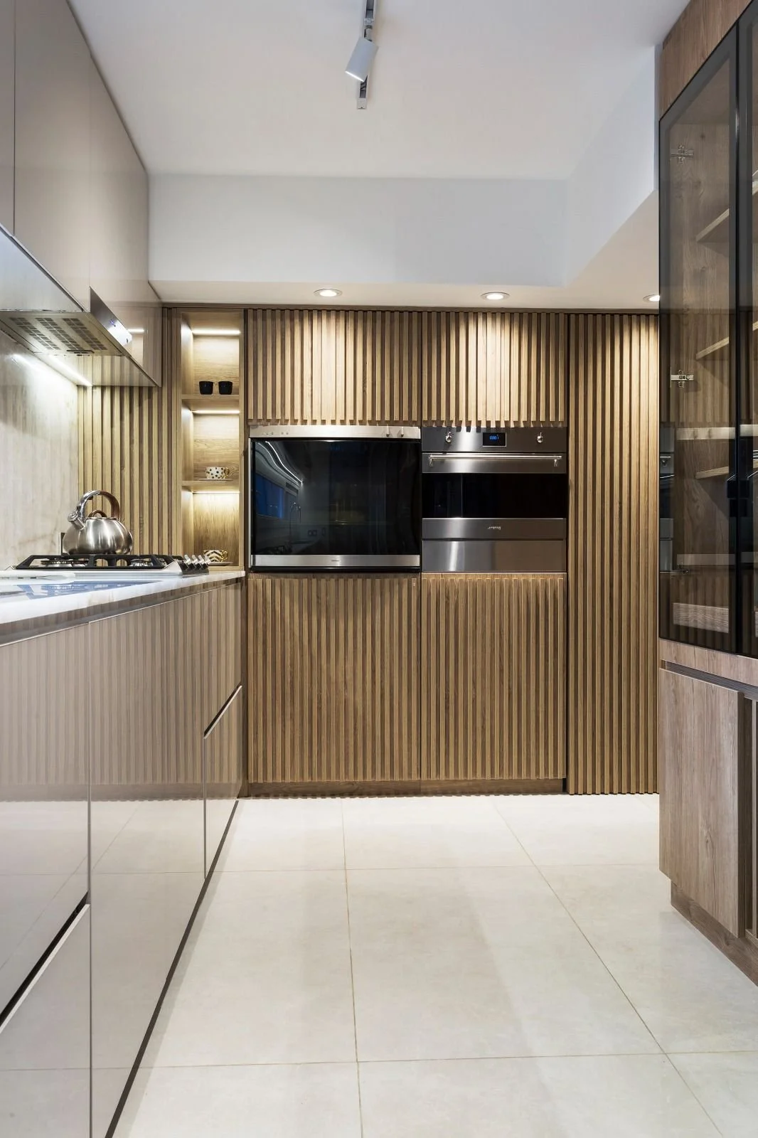 Modern kitchen with wood-paneled cabinets, built-in microwave and oven, stainless steel appliances, and a white tiled floor.
