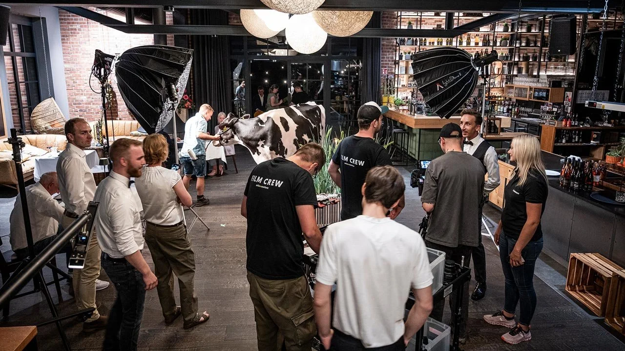 Filmset in einem Restaurant mit Lichttechnik. Im Hintergrund eine Kuh und Menschen, die für einen Dreh vorbereitet werden.  mila motions Werbefilmproduktion