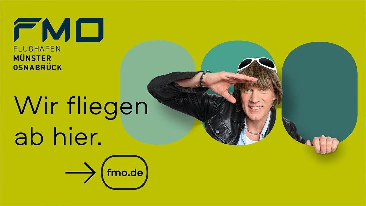 Werbung für den Flughafen Münster Osnabrück (FMO) mit einem Mann in schwarzer Lederjacke, der durch ein Loch in einem grünen Hintergrund schaut . Text: "Wir fliegen ab hier" sowie das Logo und die Website. mila motions Werbefilmproduktion