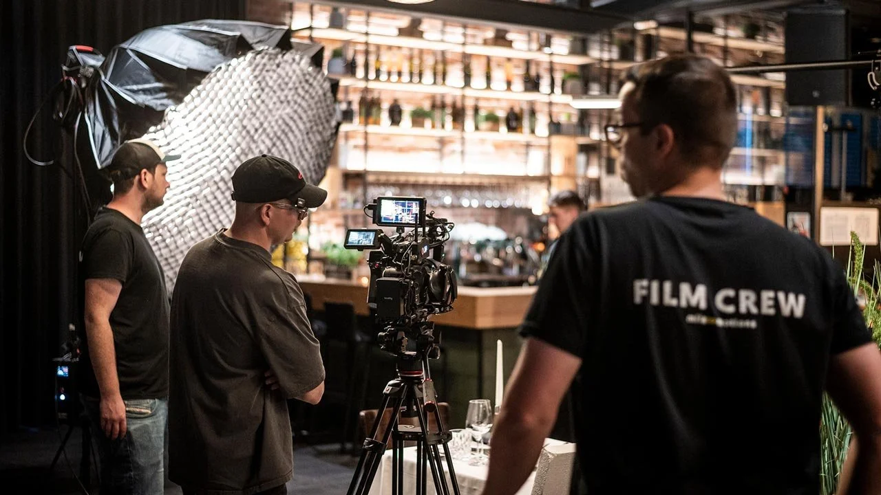 Dreharbeiten in einem Restaurant mit Filmcrew, Kamera, Beleuchtung und Barkeeper im Hintergrund. mila motions Werbefilmproduktion