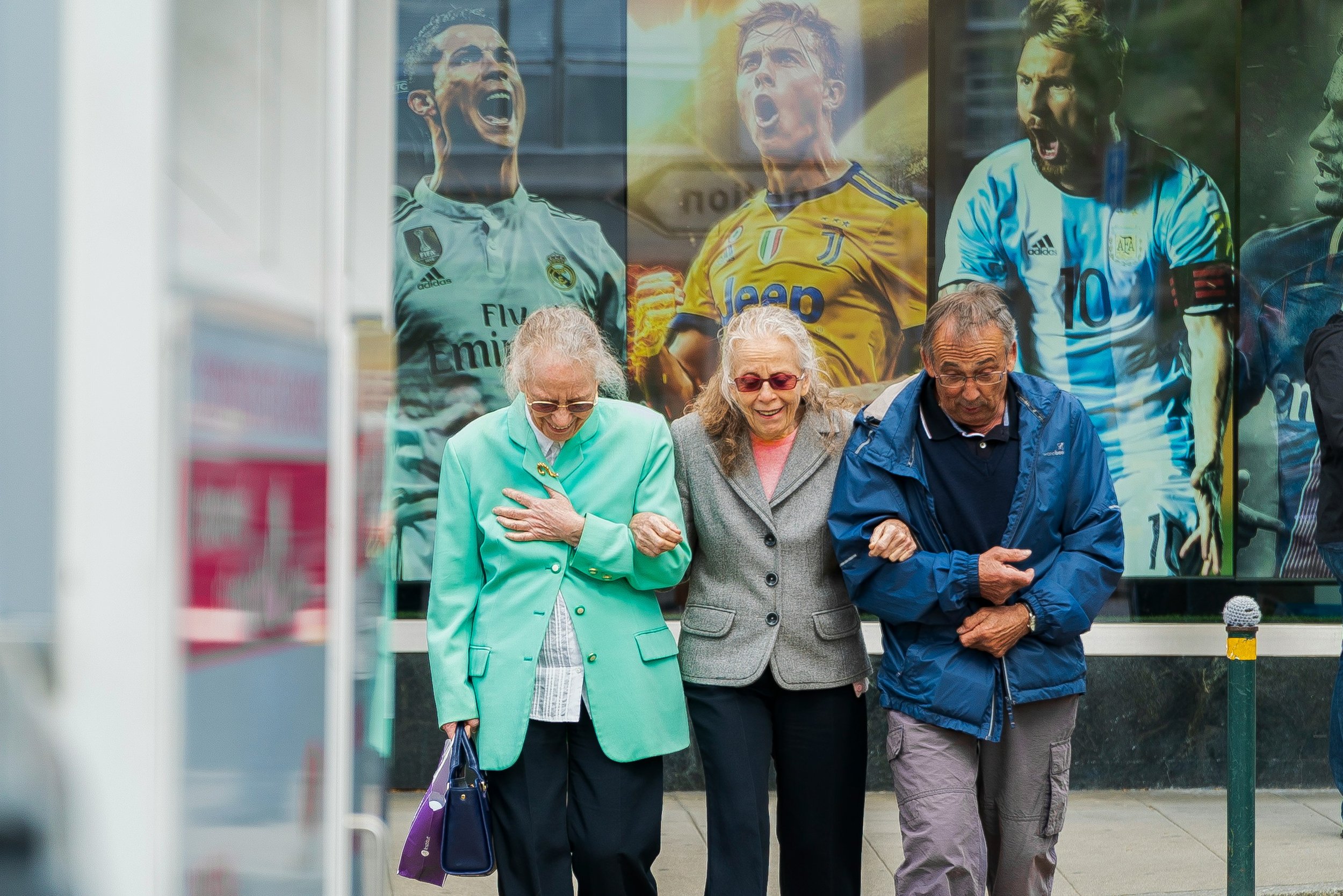 Three elderly people with linked arms crossing street together