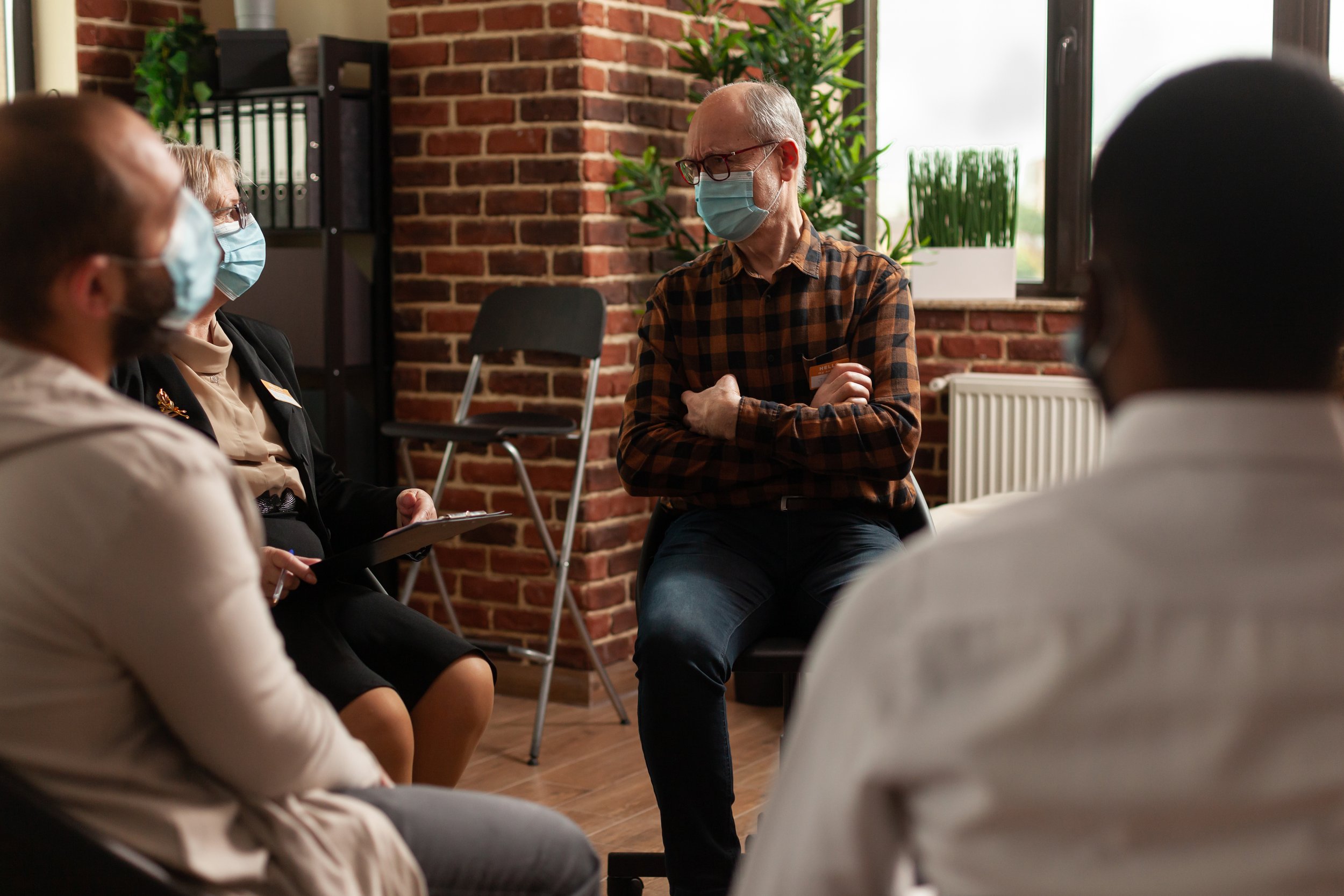 senior man with face mask talking to group of people around him