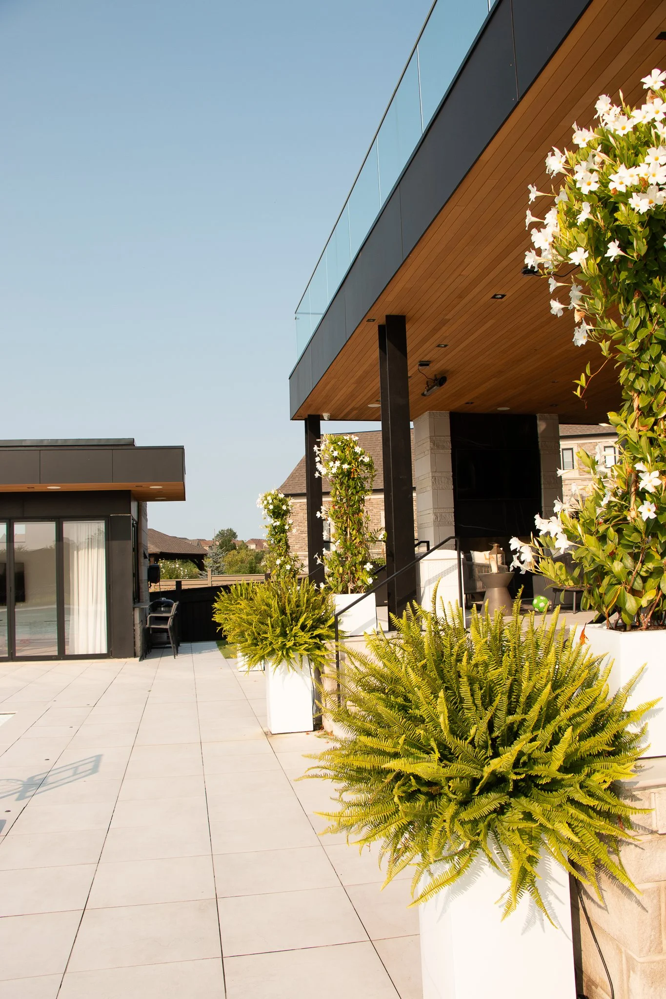 Modern outdoor patio with planters, potted plants, and a staircase leading to a covered balcony attached to a contemporary house with glass railings.