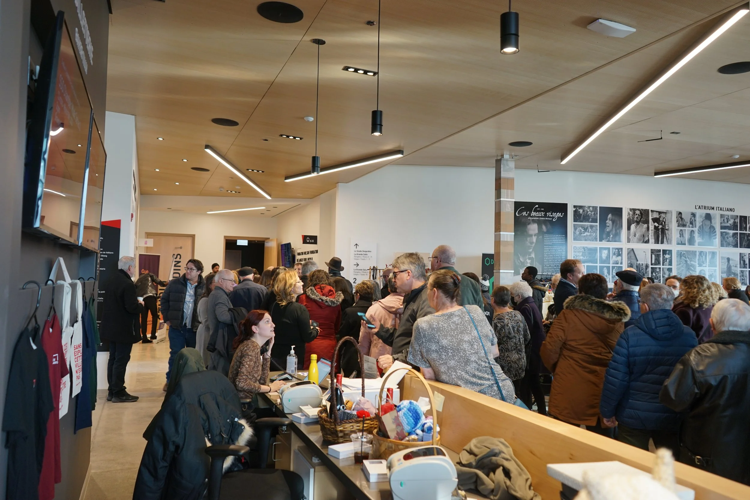 Une salle d'exposition ou de conférence très animée avec de nombreux visiteurs, certaines personnes patientent et d'autres parlent, des affiches en français sont visibles au mur.
