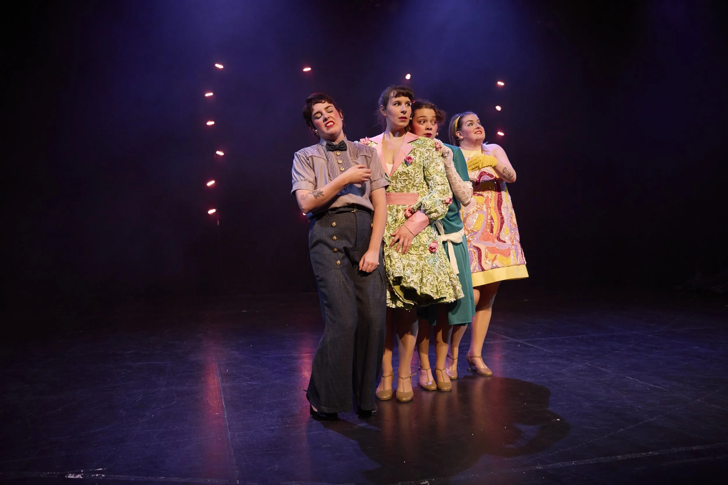 Créations In Vivo. Quatre femmes en costumes vintage sur une scène de théâtre avec un fond sombre et des lumières