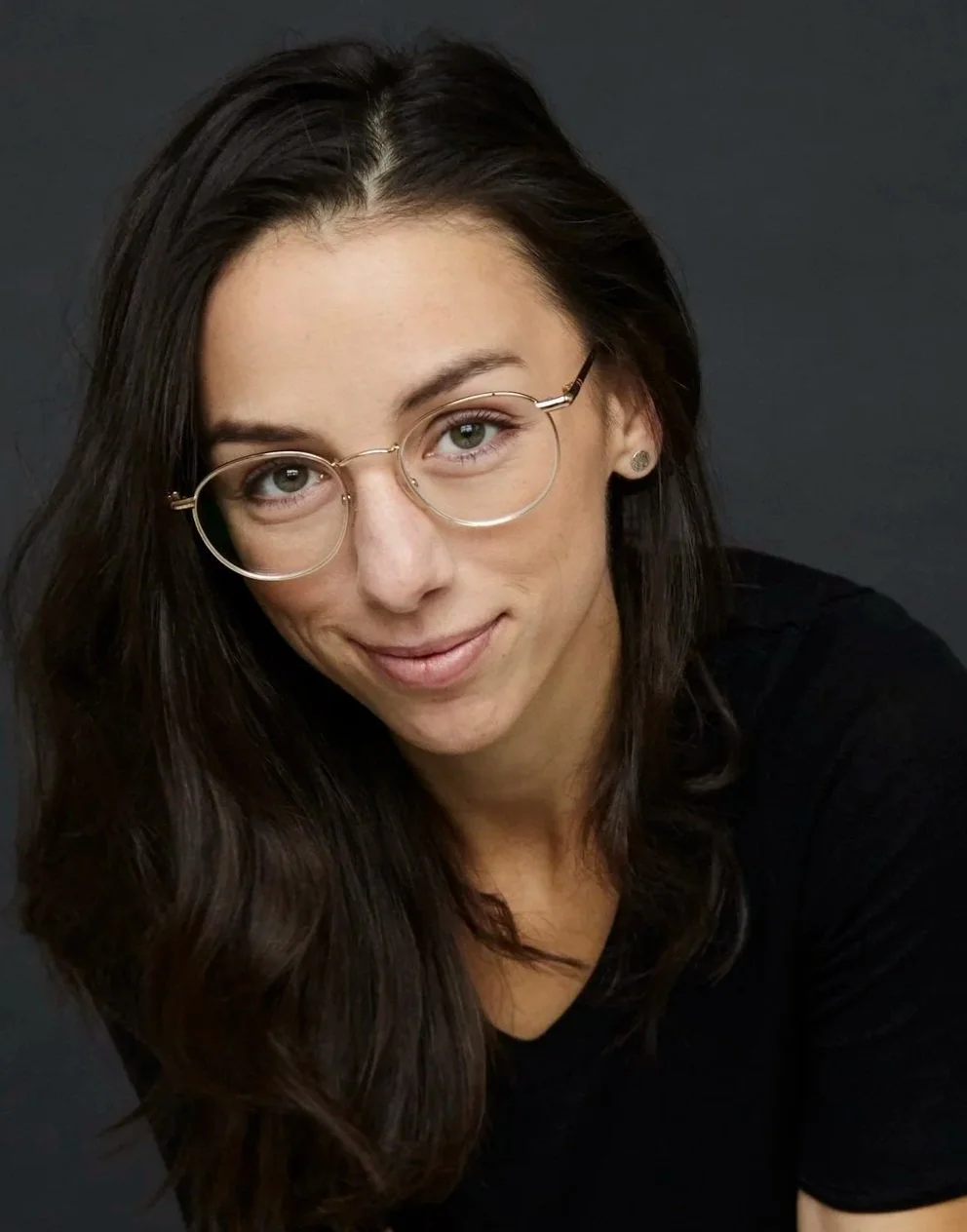 Marie-Claire Marcotte. Une femme avec des cheveux longs et bruns, portant des lunettes rondes, souriant légèrement, portant un haut noir, contre un fond sombre.