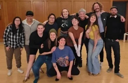 Créations In Vivo. Groupe de dix personnes posant ensemble dans une salle avec un mur en bois et des guirlandes lumineuses.