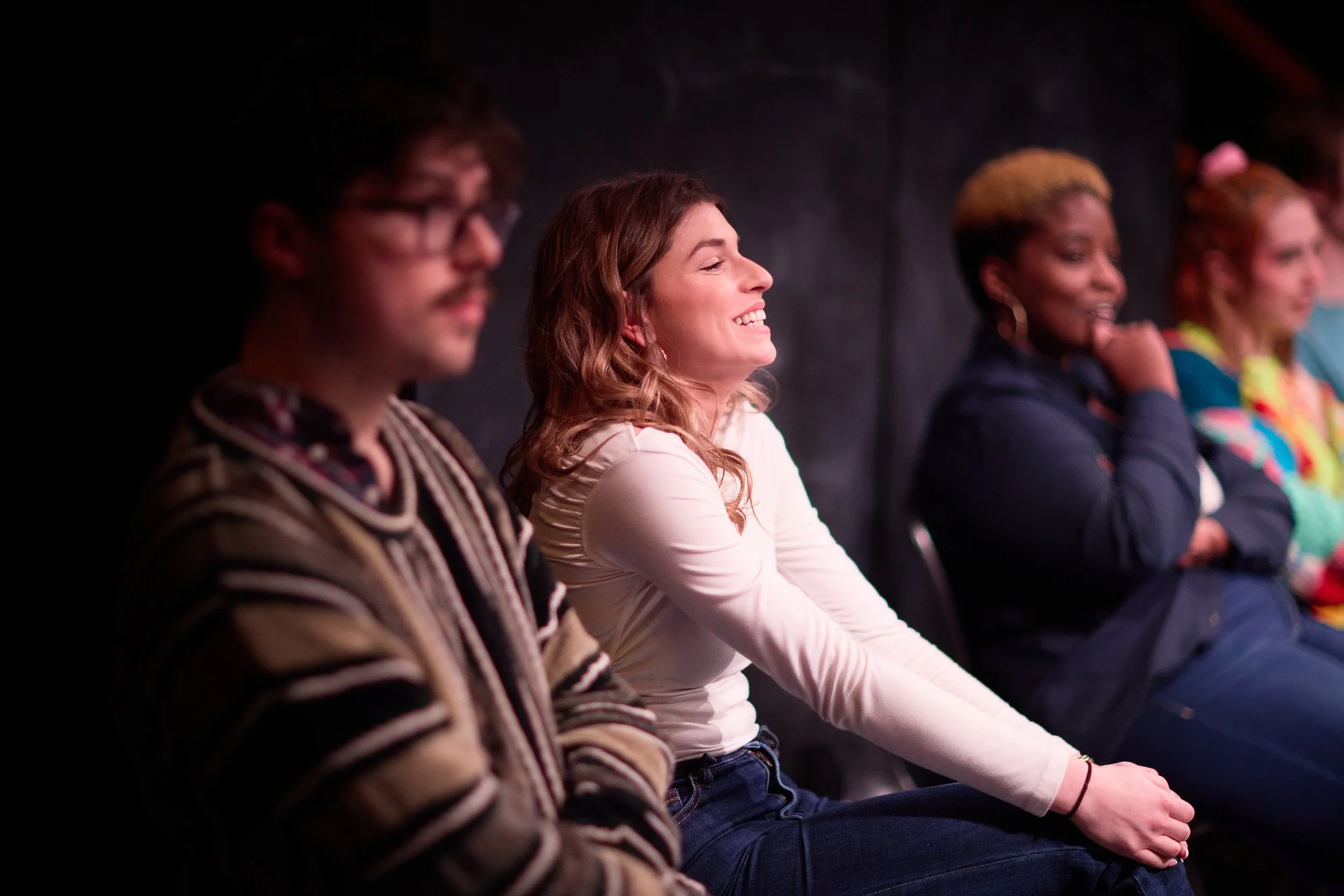 Groupe de personnes assises sur une scène, riant et souriant, lors d'une performance ou d'un spectacle.