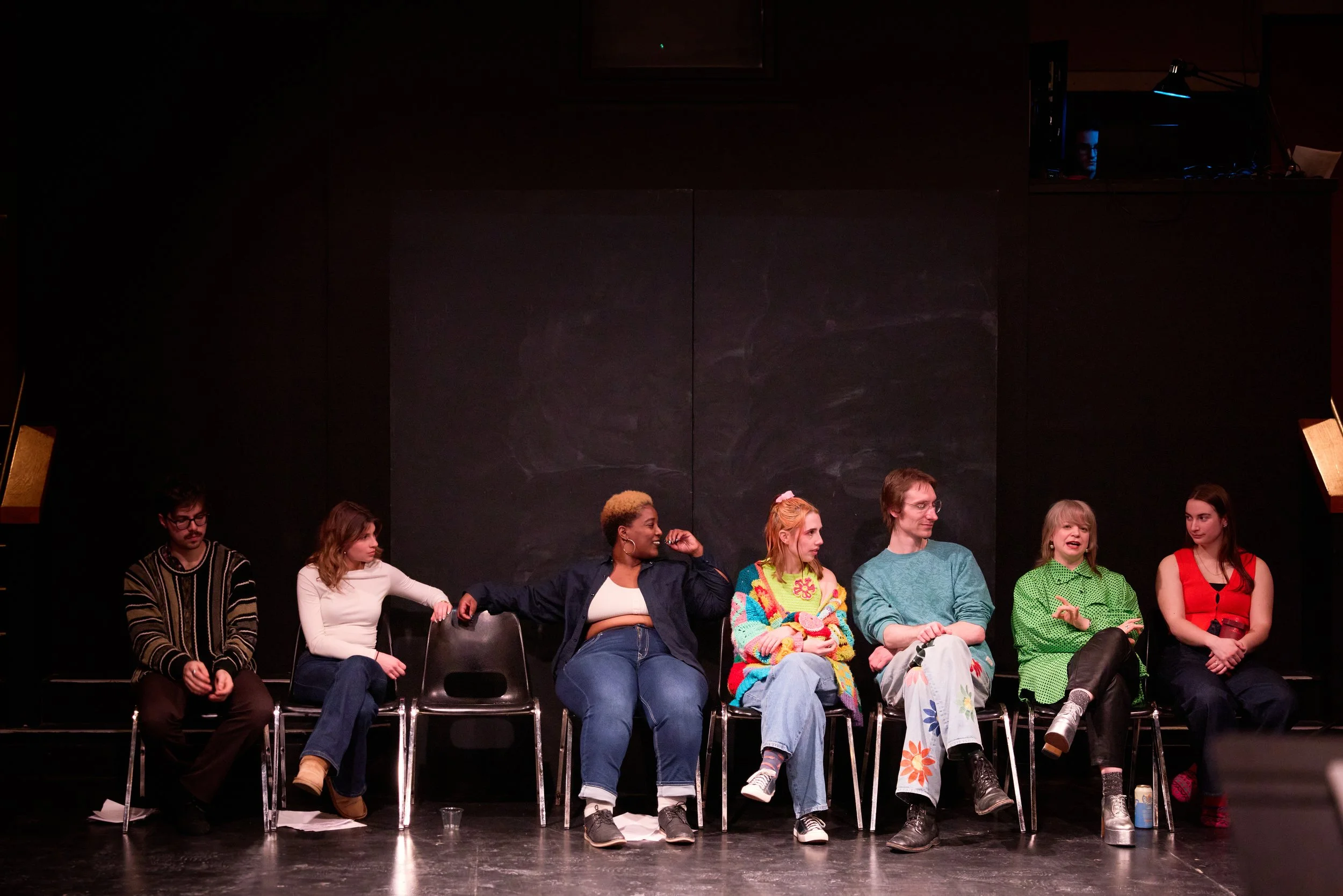 Groupe de sept personnes assises sur des chaises sur scène, en train de discuter.