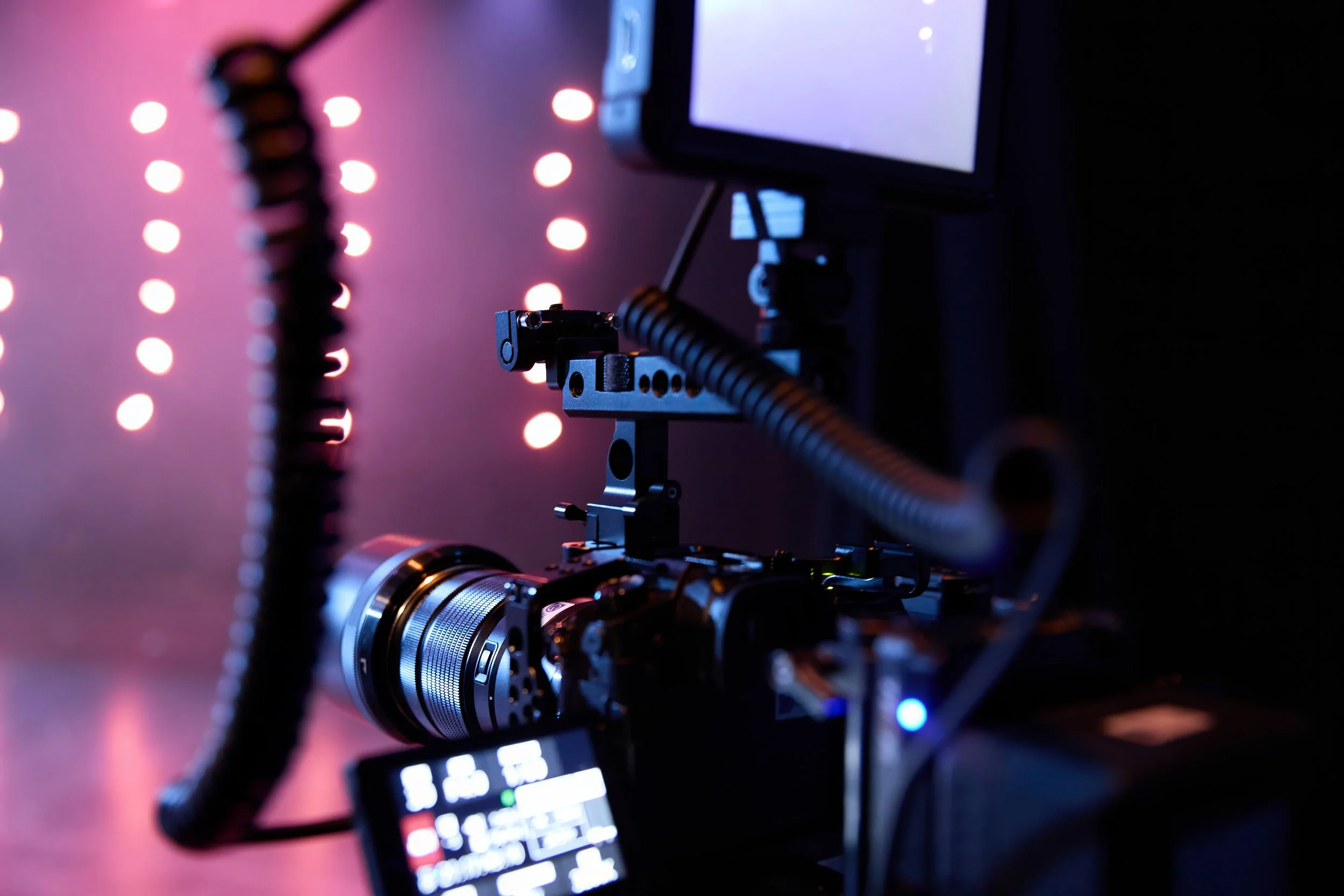 Une caméra professionnelle de cinéma en gros plan, préparée pour un tournage, avec un écran de contrôle à l'écran montrant des options de réglage, dans un environnement sombre avec des lumières colorées en arrière-plan.