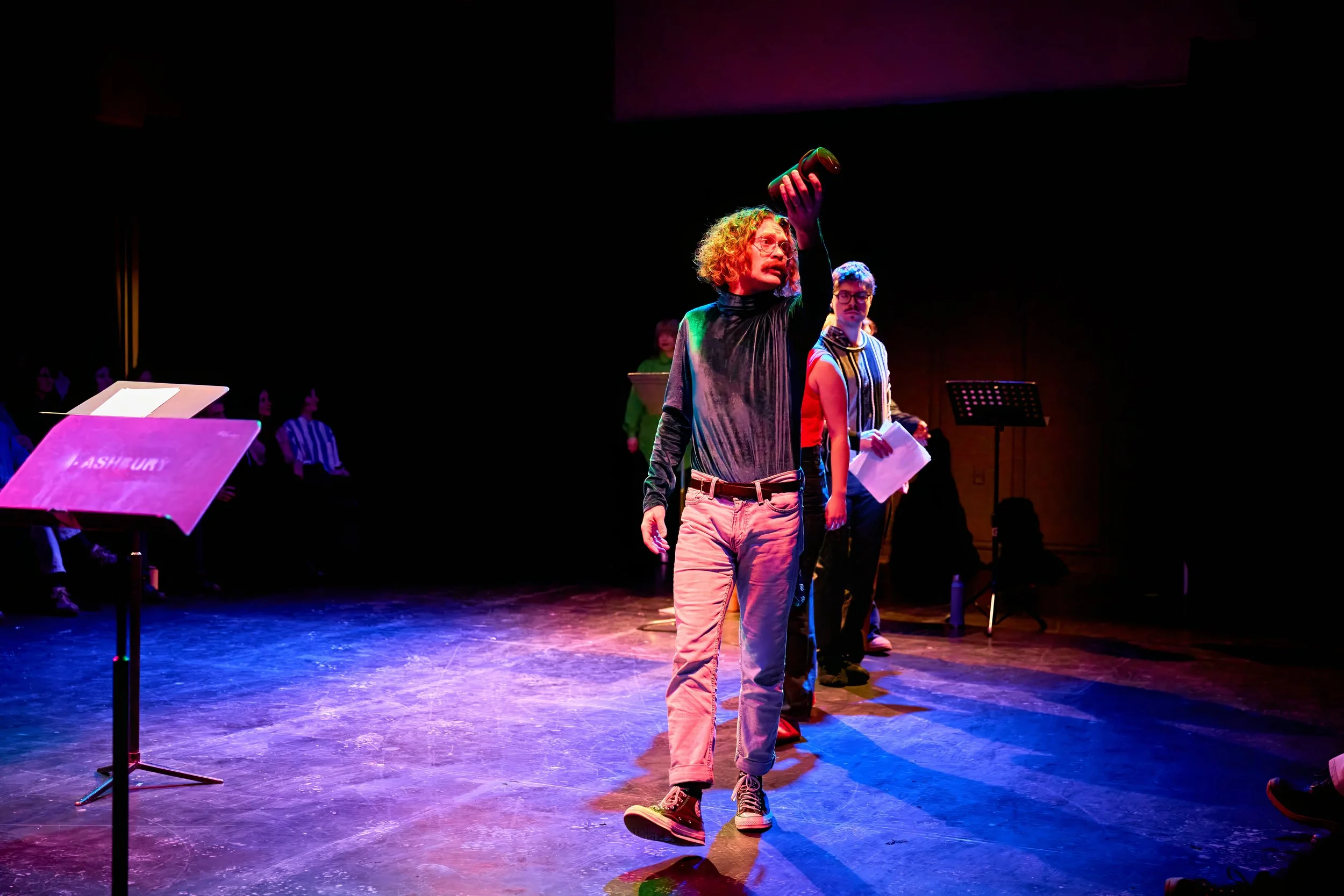 Personnages en costume sur scène pendant une performance théâtrale ou un spectacle, avec un décor sombre et des éclairages colorés.