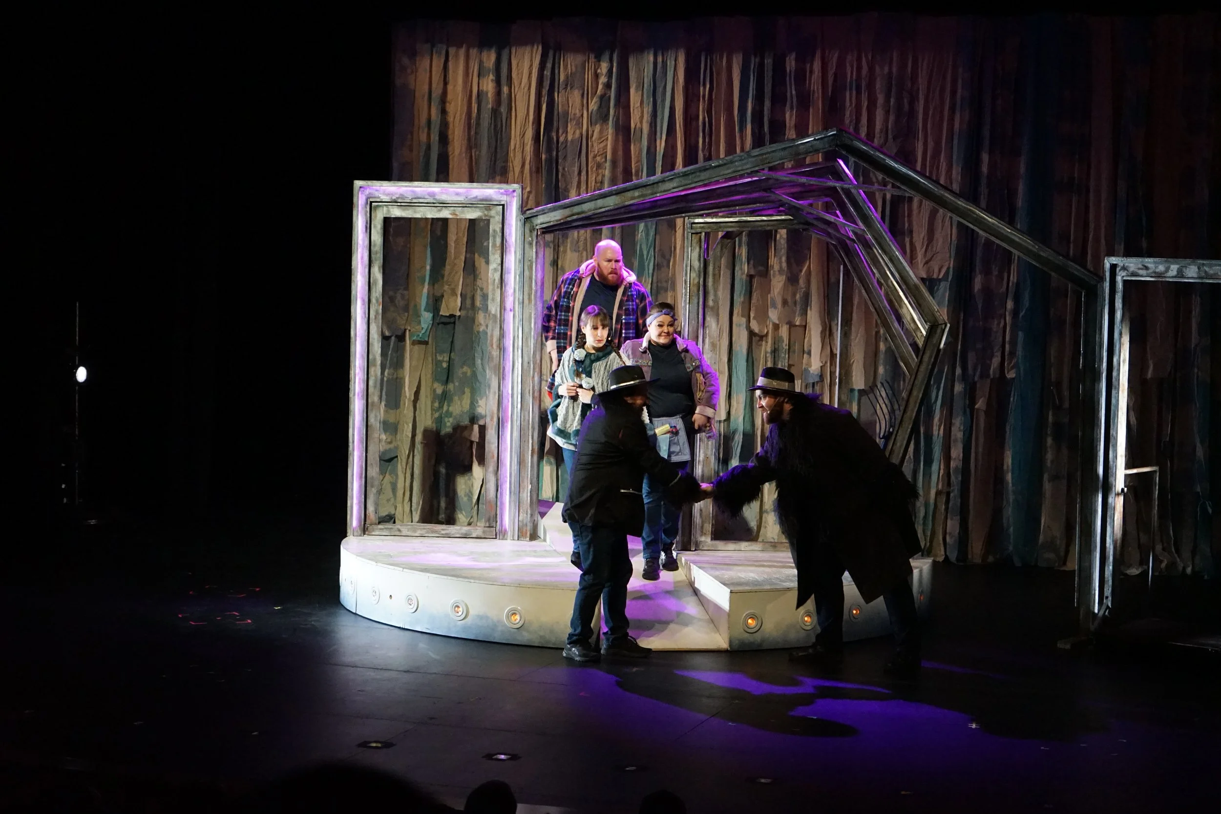 Scène de théâtre avec plusieurs acteurs sur une scène minimaliste, échangeant une poignée de main, dans une mise en scène moderne.