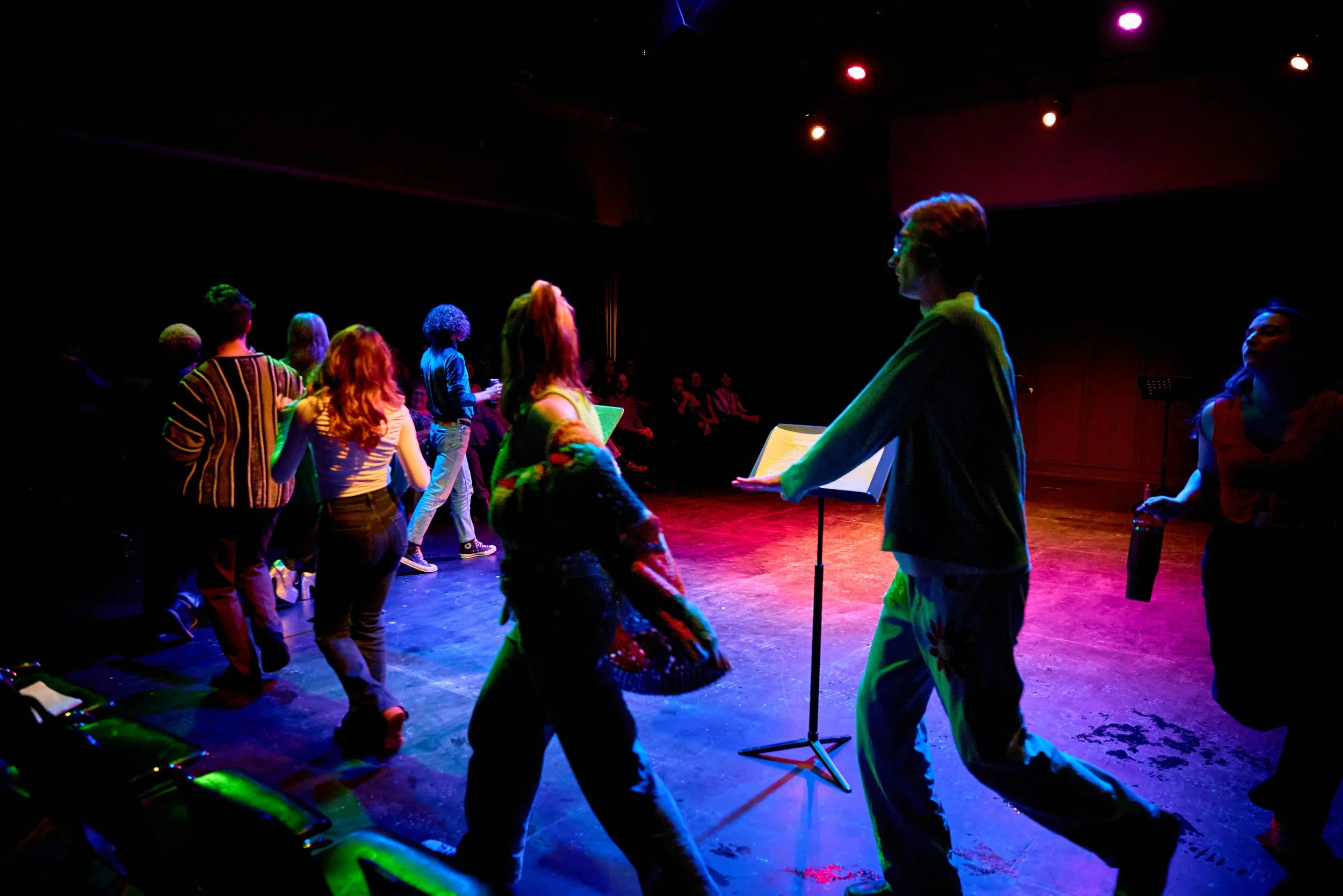 Groupe de personnes dansant sous des lumières colorées sur une scène de théâtre ou de studio
