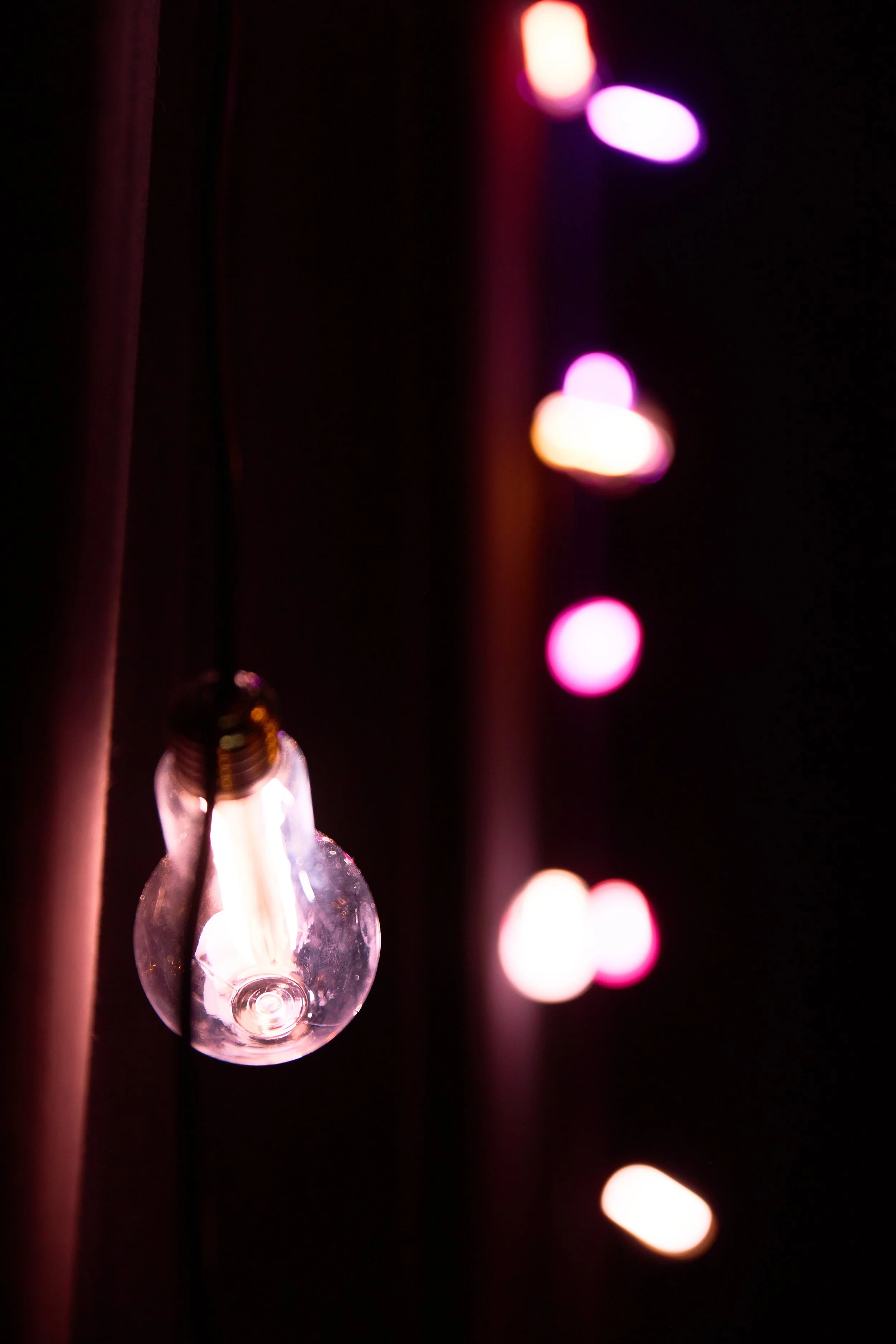 Ampoule électrique non allumée avec des guirlandes de lumières colorées floues en arrière-plan