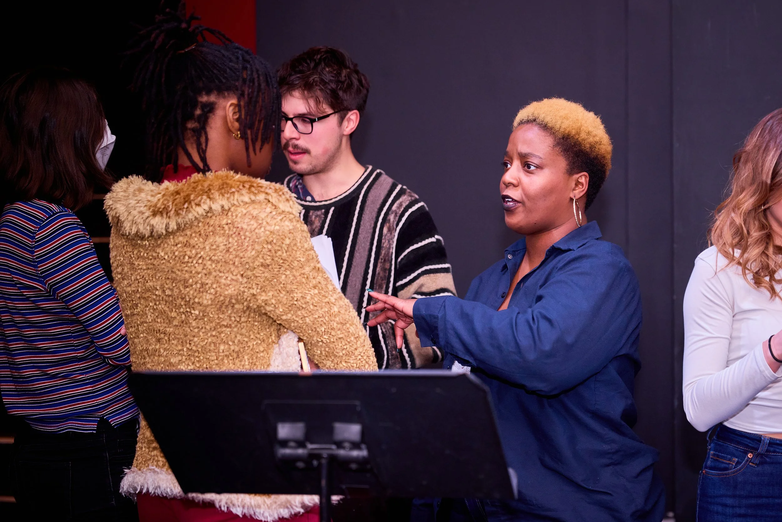 Groupe de personnes en discussion, la femme noire en bleu expliquant quelque chose à un groupe.