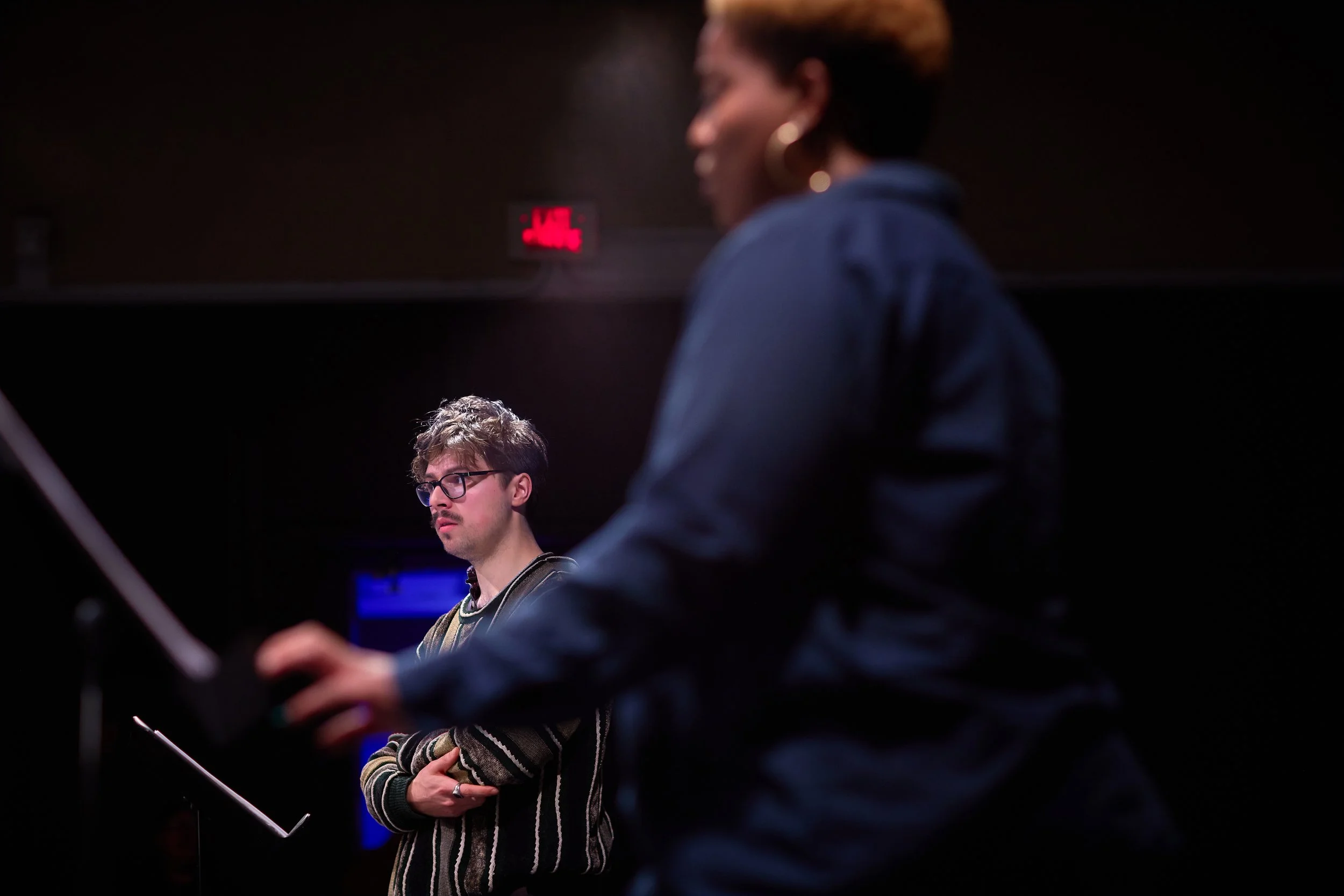 Deux personnes en studio d'enregistrement ou en répétition, l'une avec des lunettes, une maison d'enfance, et l'autre avec des cheveux courts, en train de jouer de la musique ou de pratiquer un instrument.