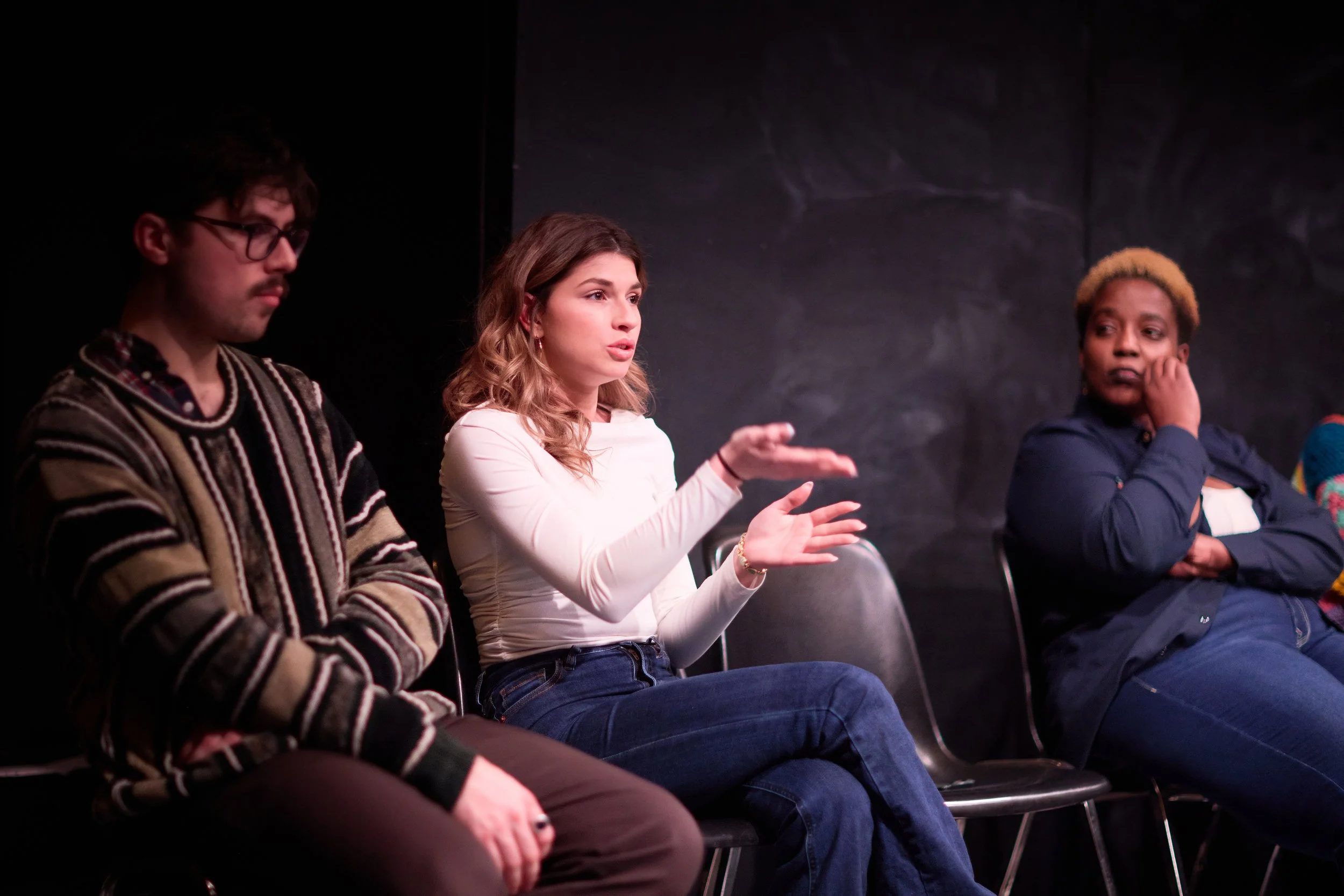 Trois personnes en discussion lors d'une réunion ou atelier, assises en ligne face à un mur noir.