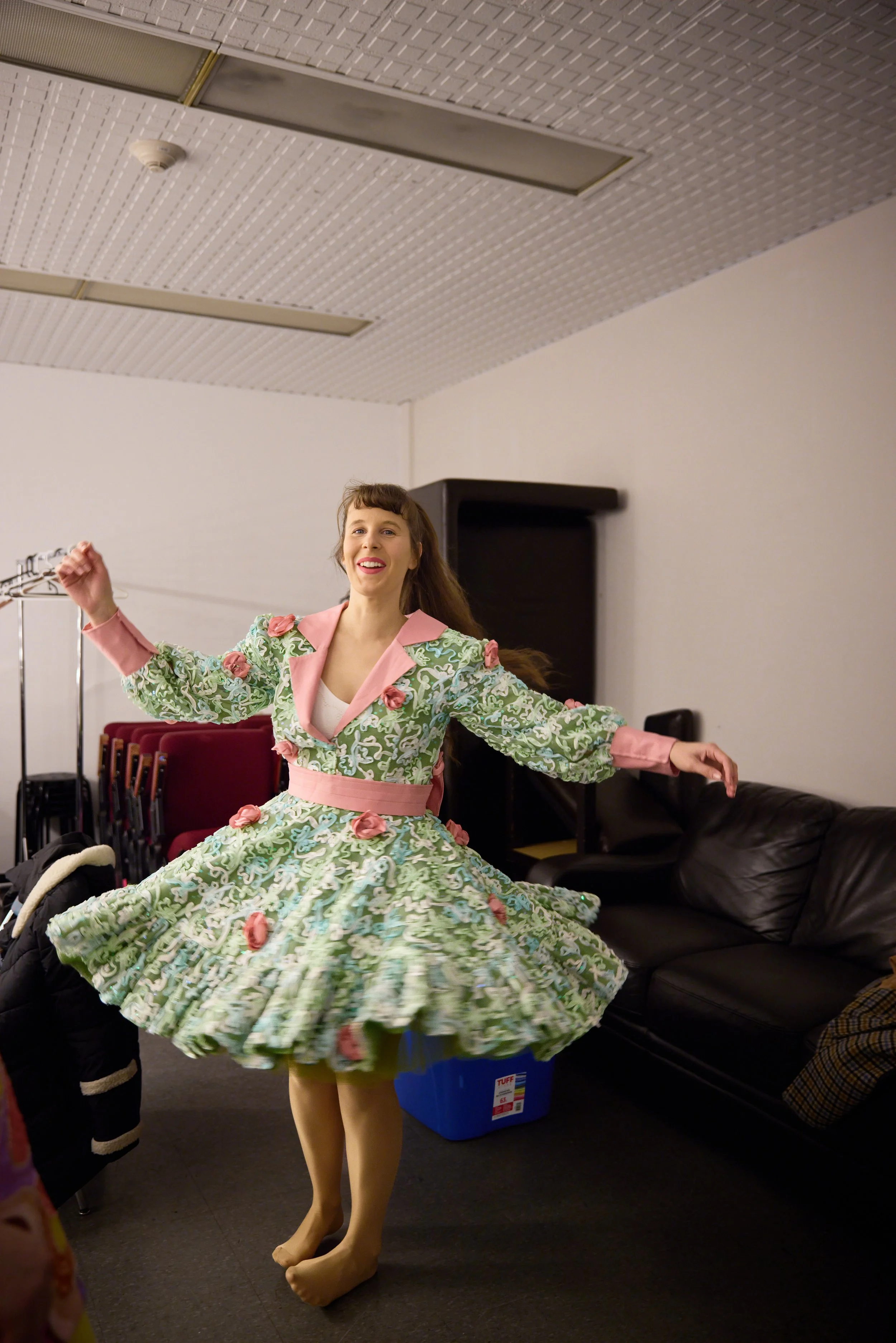 Une femme souriante en robe colorée en train de danser dans une pièce avec un canapé noir