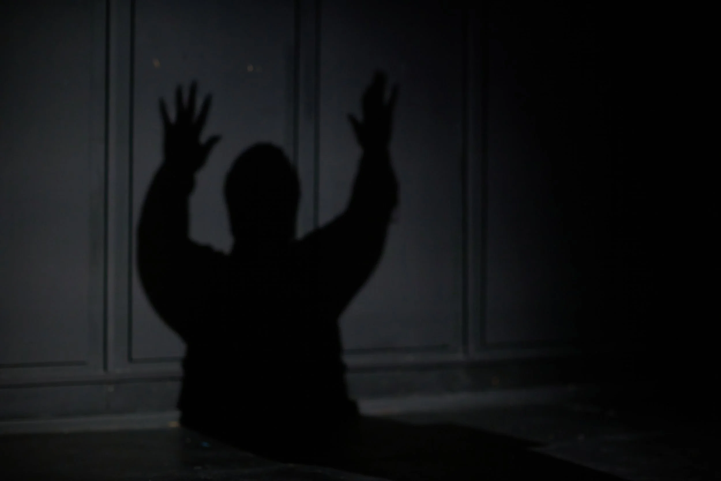 Silhouette d'une personne contre un mur sombre, avec les mains levées.